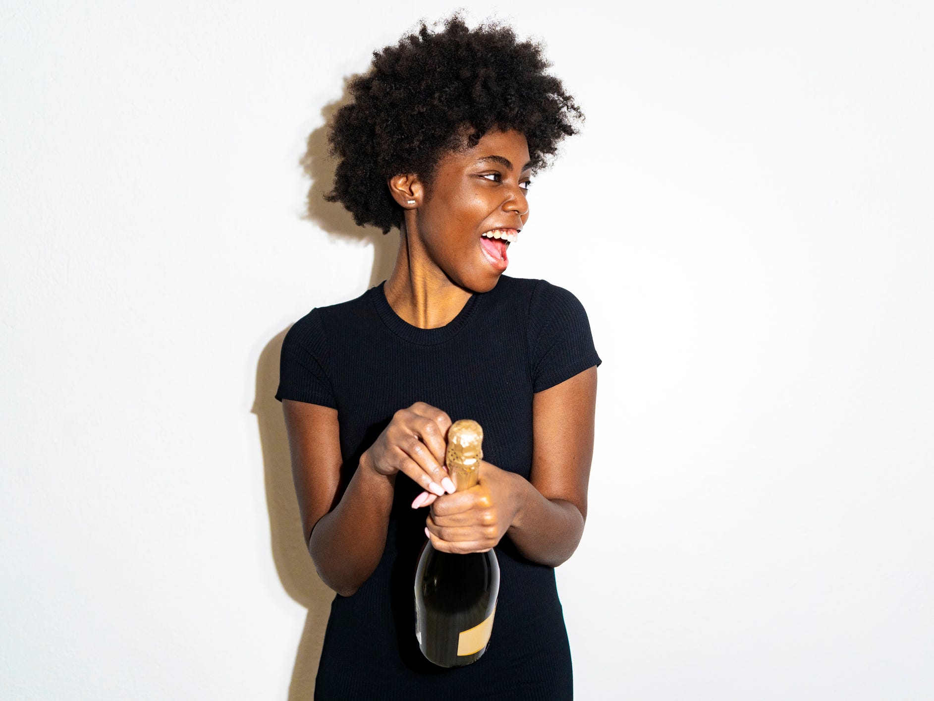 A woman opening up a bottle of Champagne against a white background.