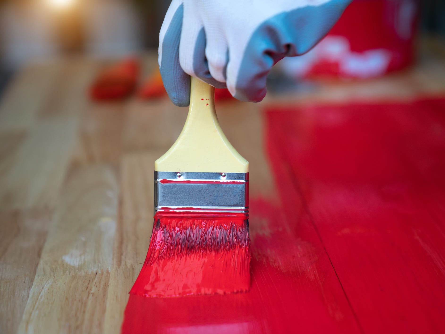 A closeup of a hand painting wood red