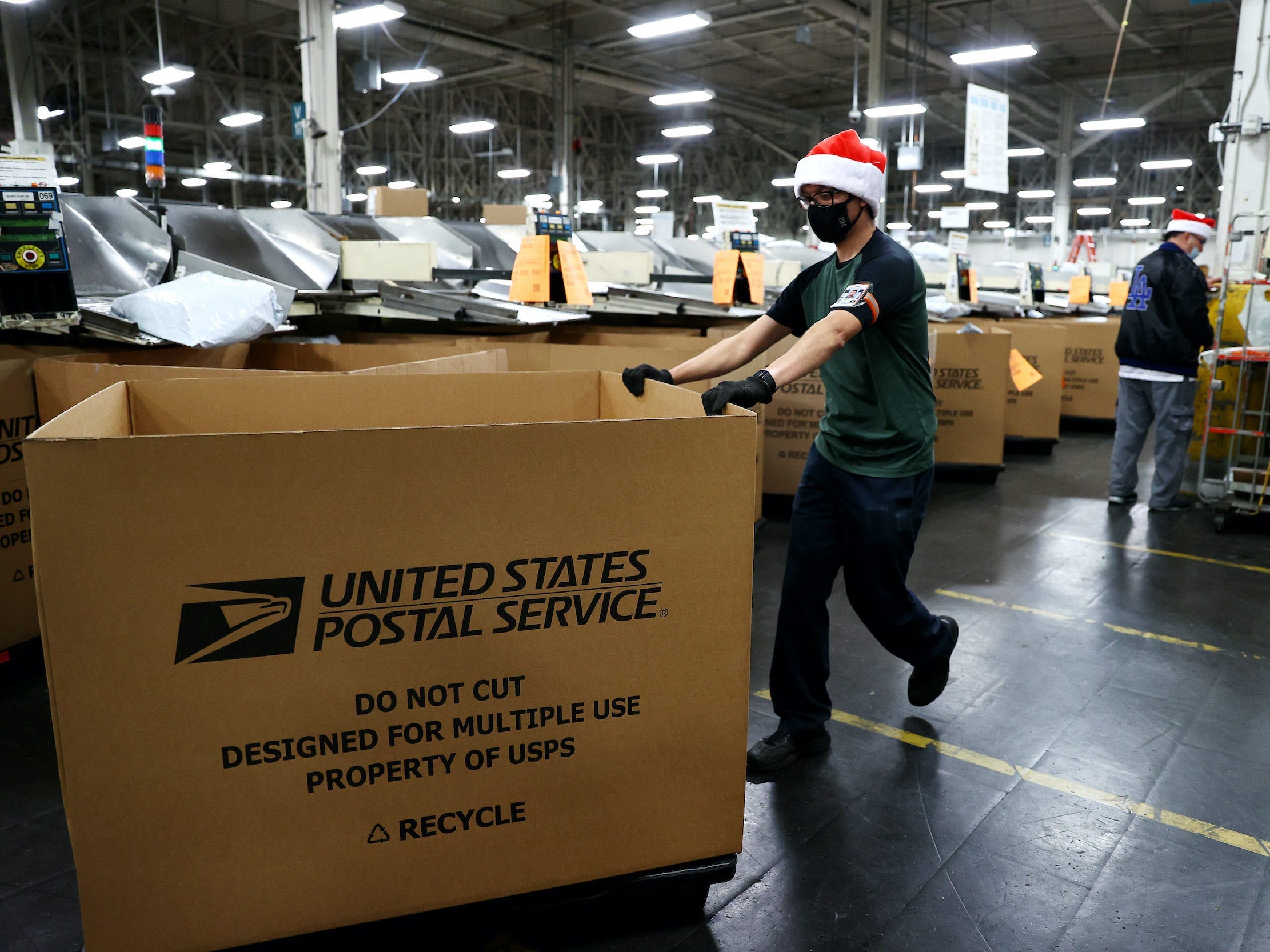 US Postal Service employee pushes large box in warehouse while wearing Santa hat