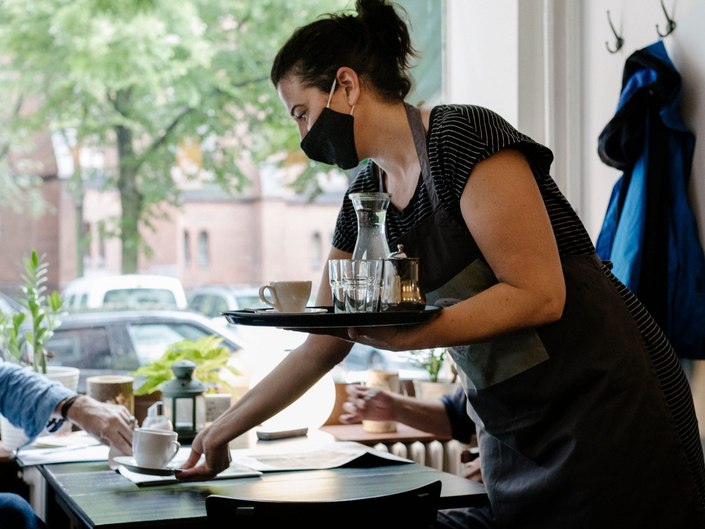 A waitress wearing a face mask and serving a customer some coffee at his table in a restaurant.