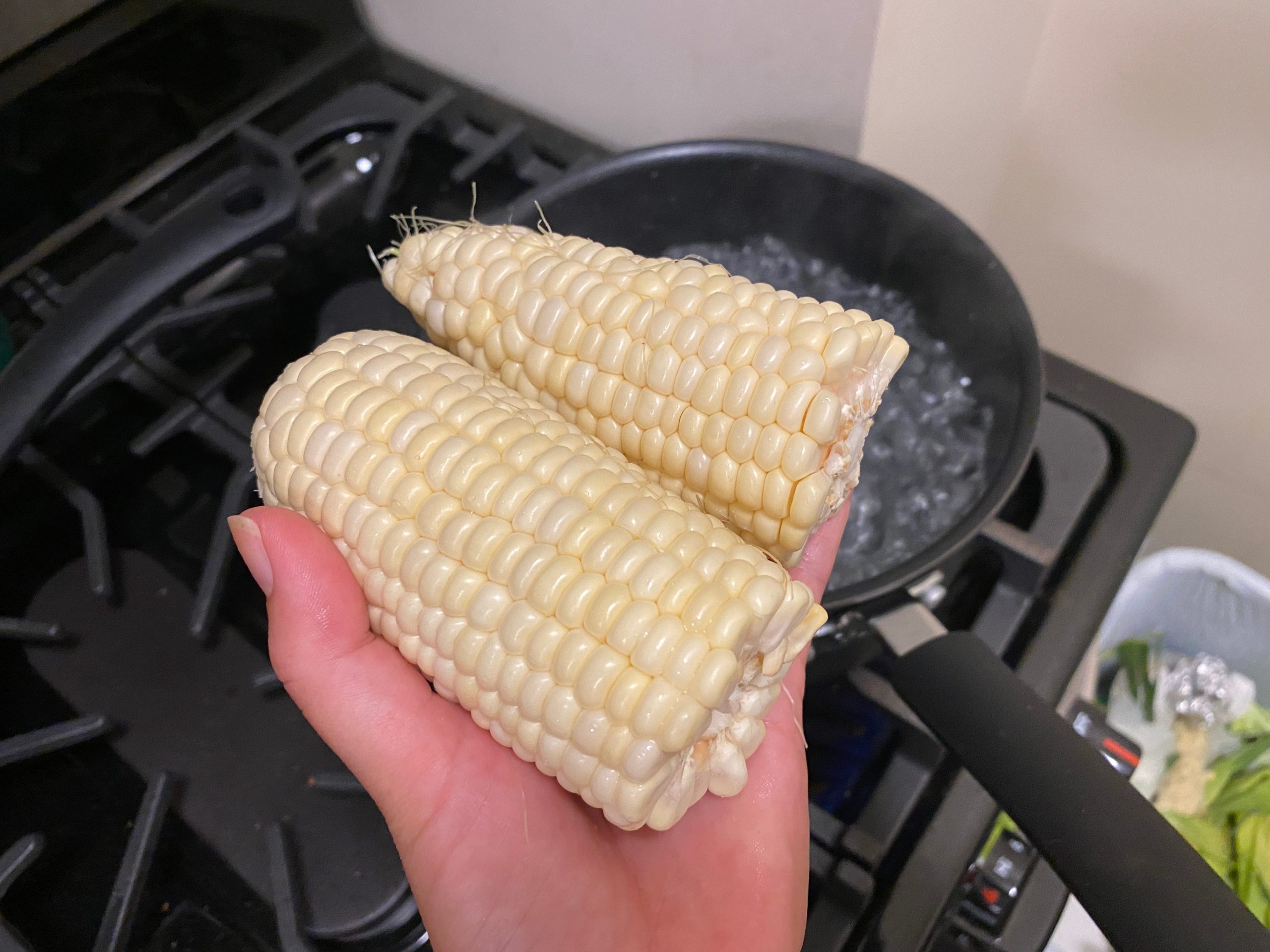 Corn on the cob over a boiling pot.