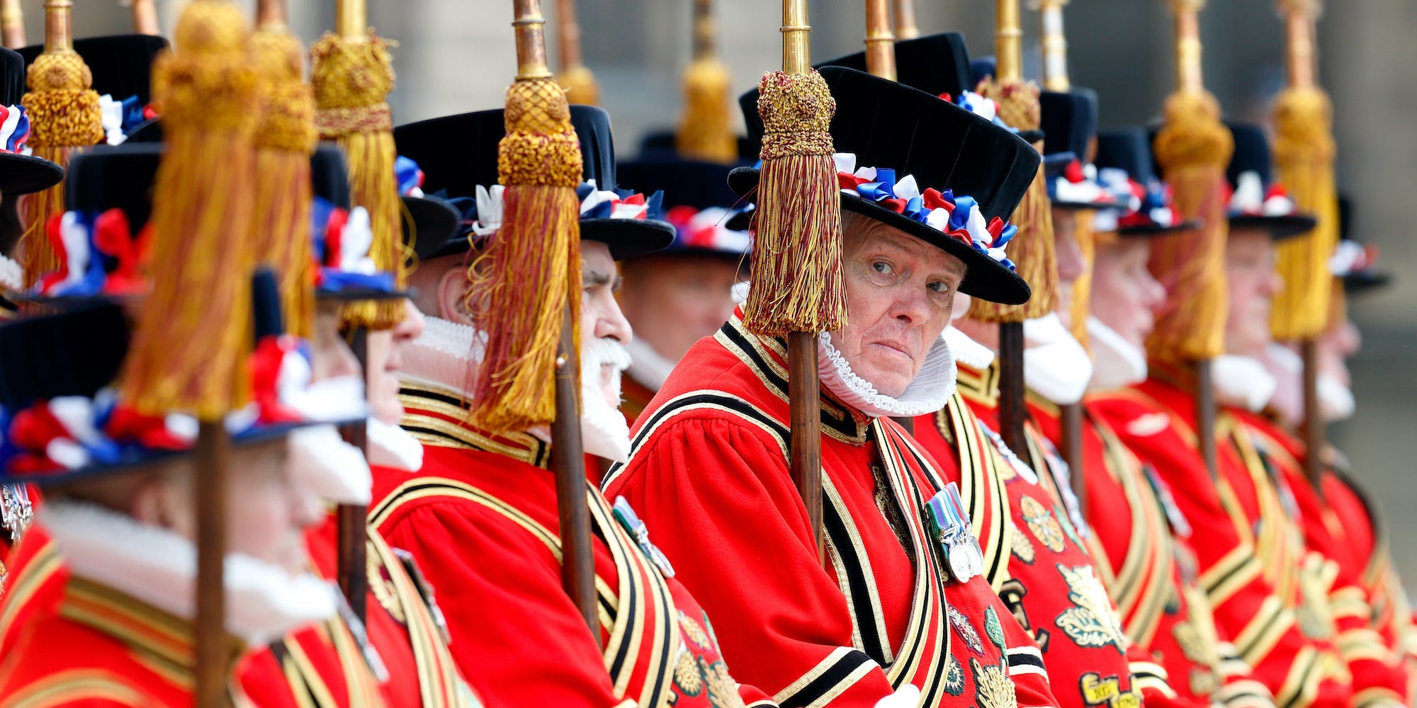 A side view of several Yeomen of the Guard in full red regalia at a royal event. One man peers sideways.