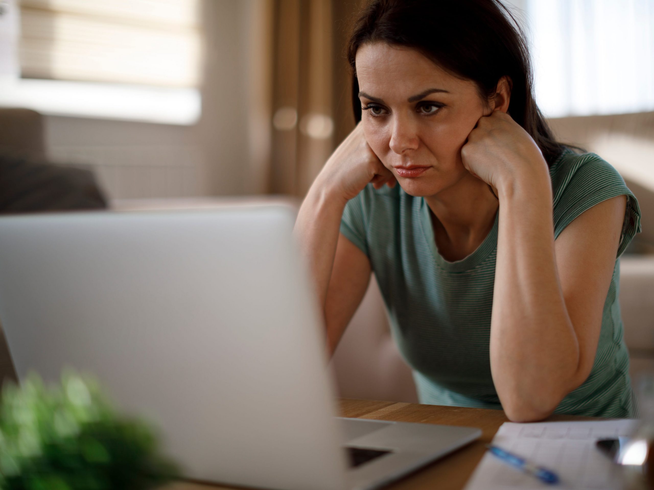 A woman looks sad as she stares at her laptop.