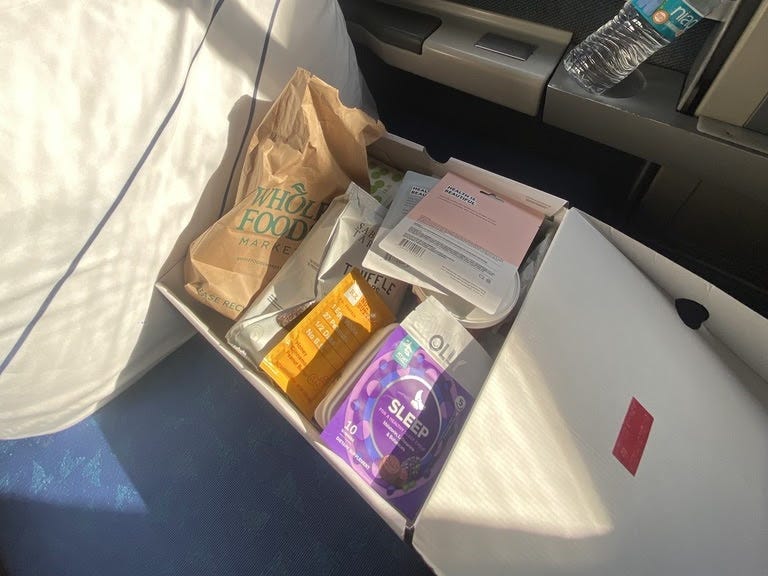 A box filled with tea, food, and masks on an Amtrak seat.