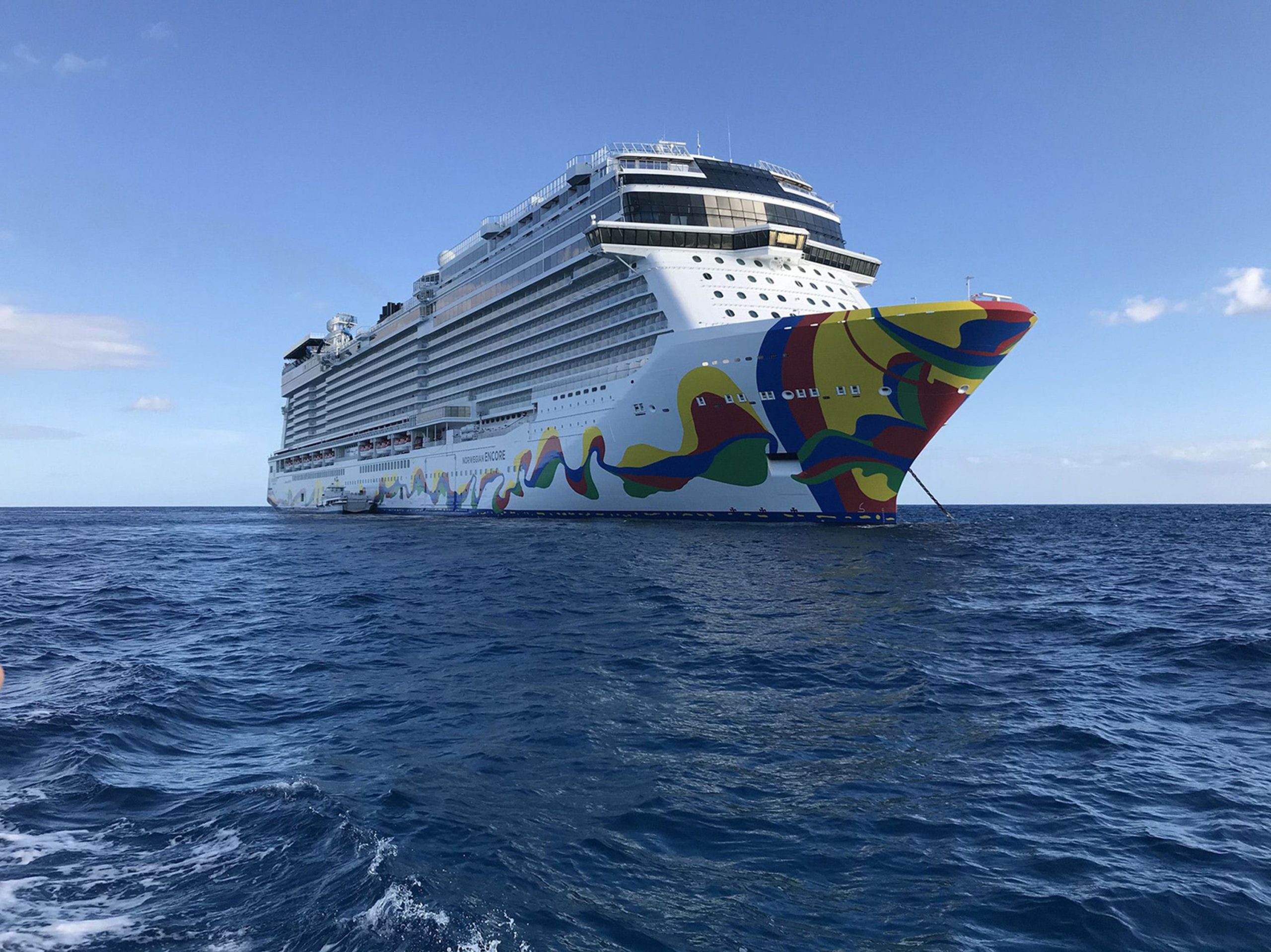 A Norwegian Cruise Lines ship with a colourful side sets sail on a sunny day.