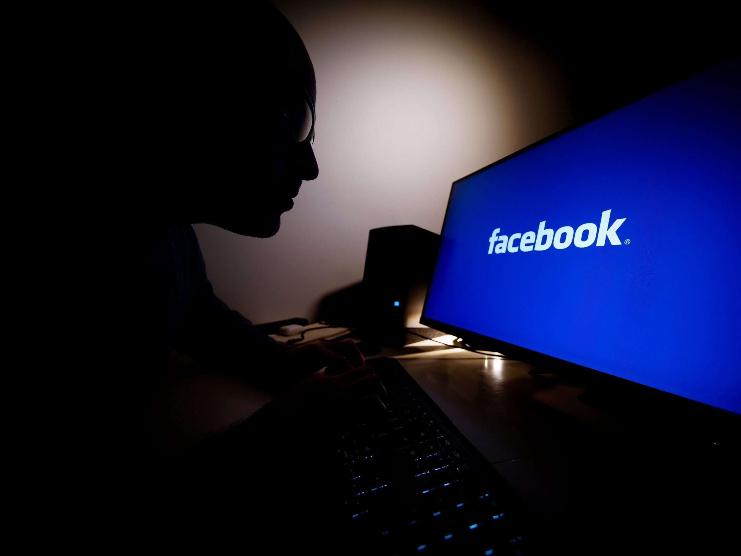 A man looks at a computer screen with the Facebook logo