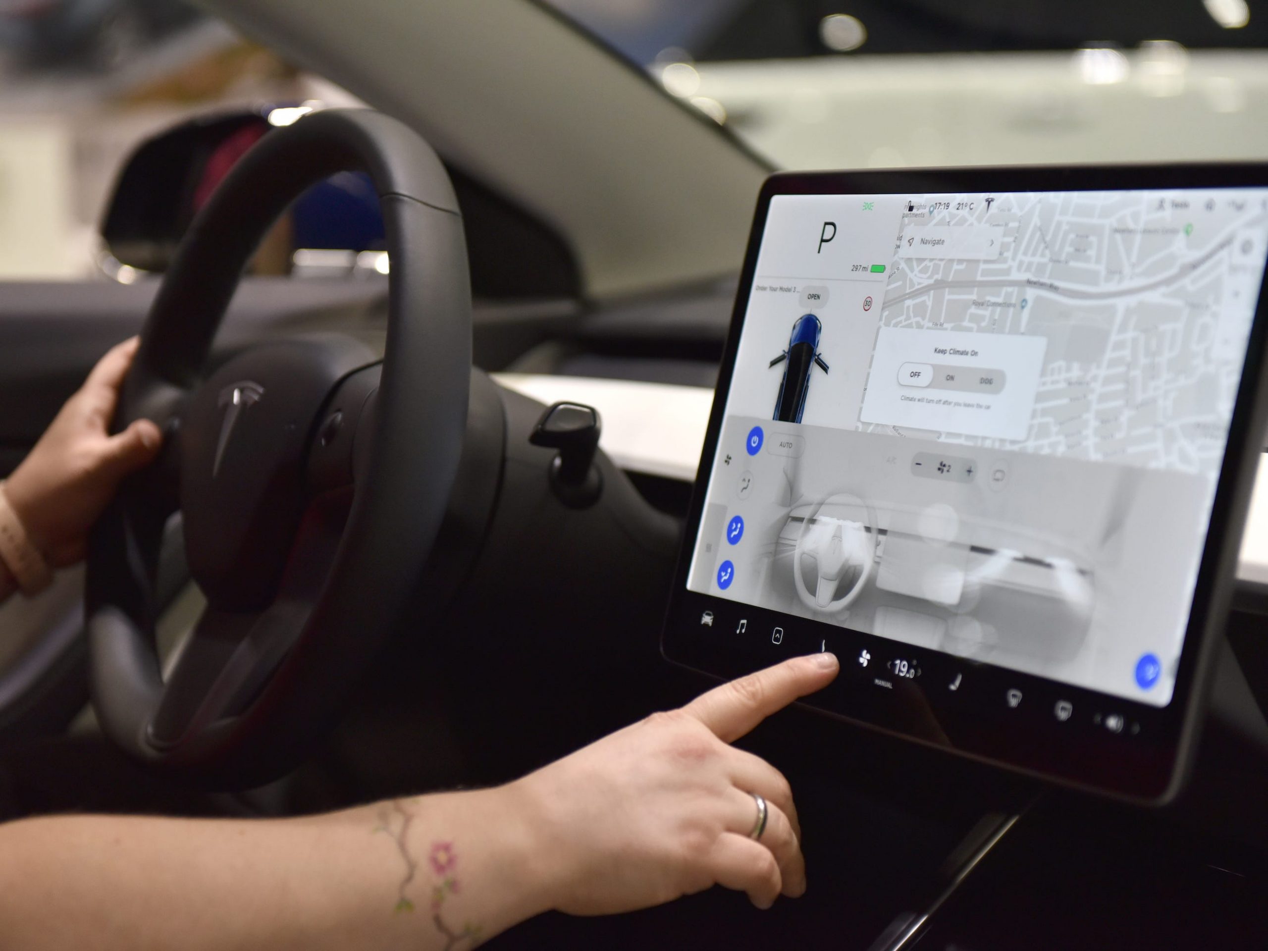 A person holds the wheel of a Tesla and operates the touchscreen.