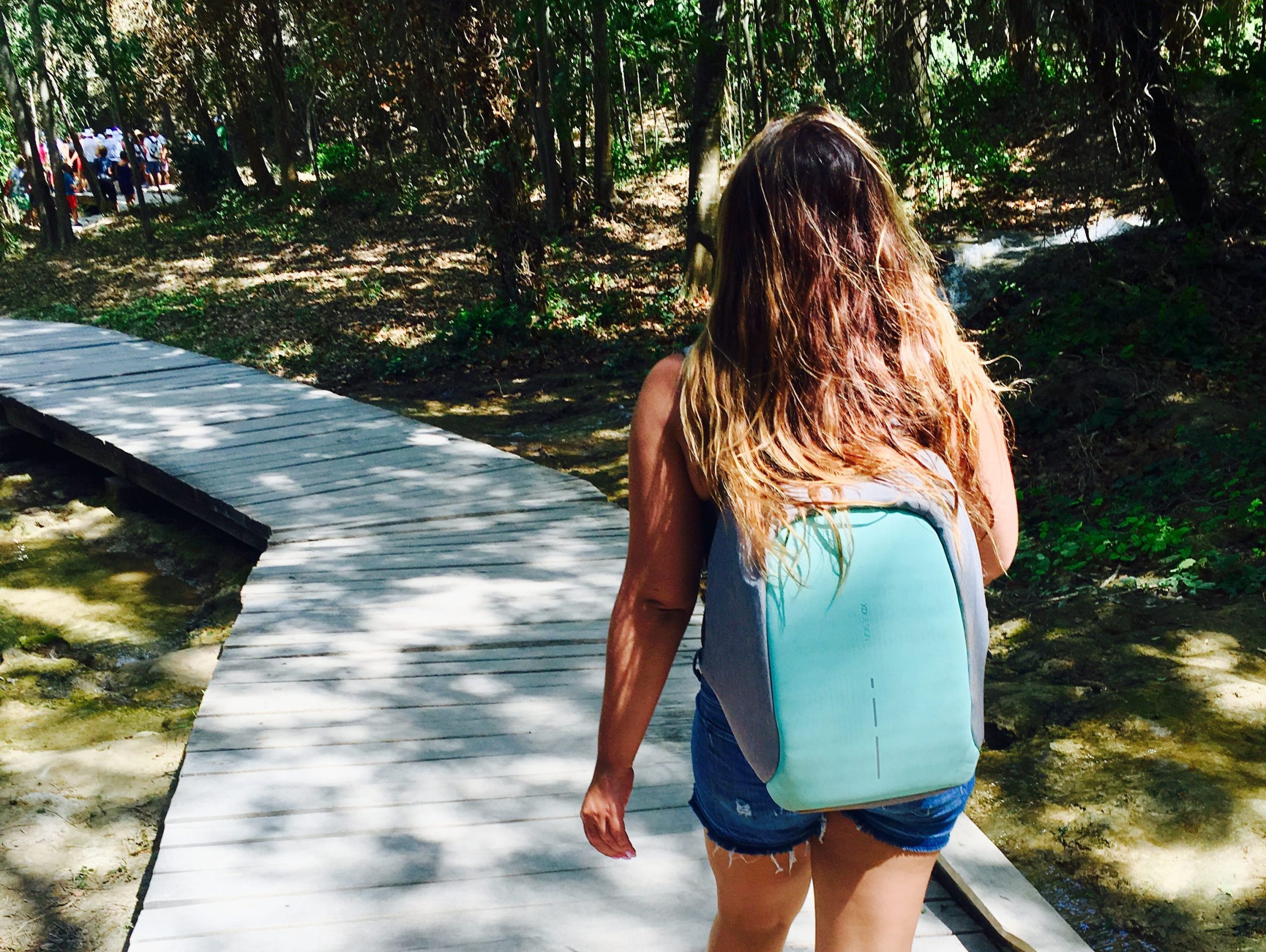 the writer with a backpack walking through trees on a path