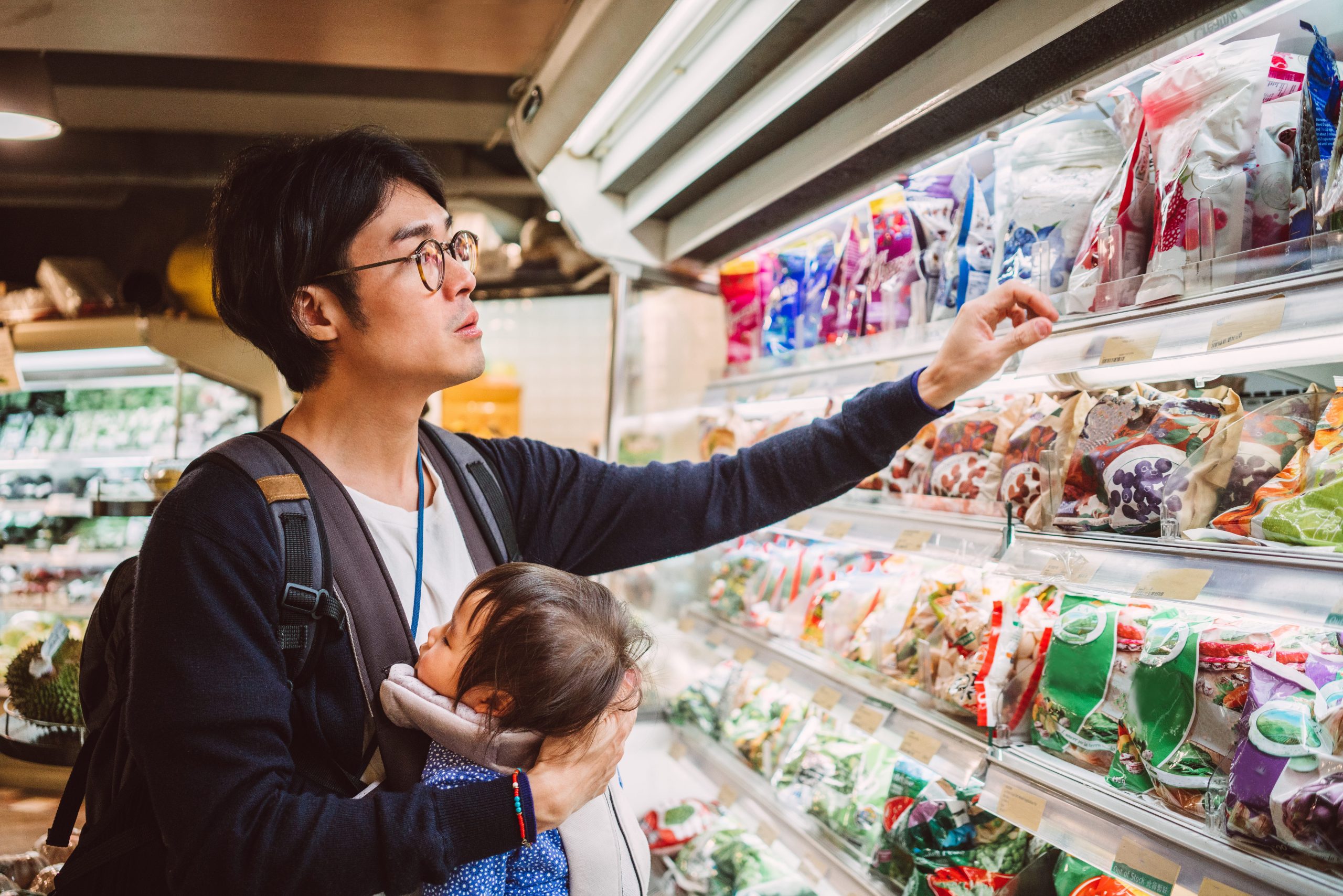 An Asian man holding a baby shops for items in the supermarket