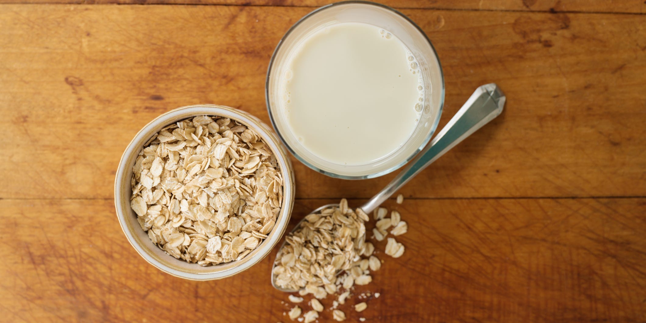 Overhead shot of a jar of oats, a spoon full of oats, and a glass of milk.