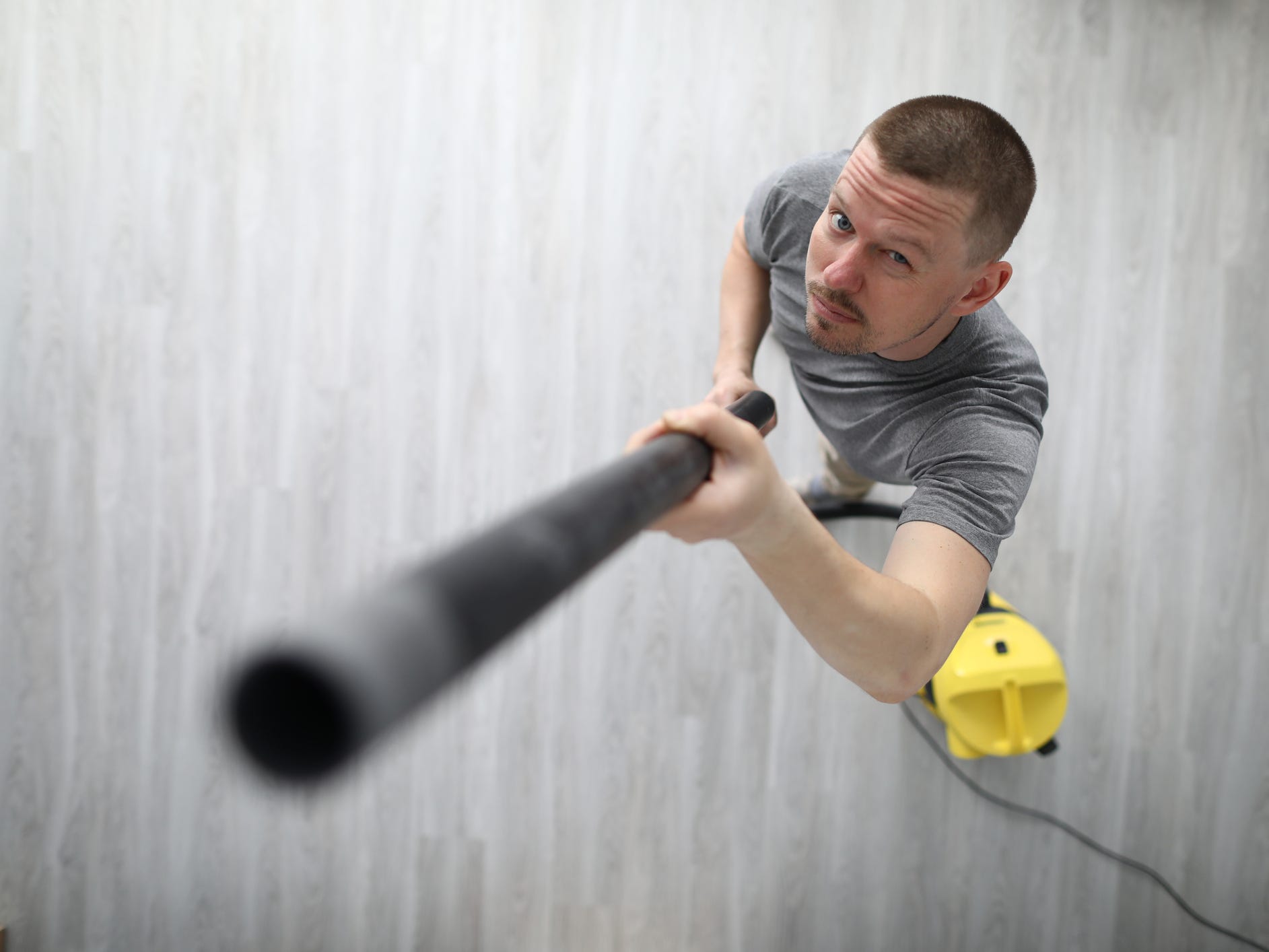 A view from above of a man using a vacuum hose to vacuum cobwebs