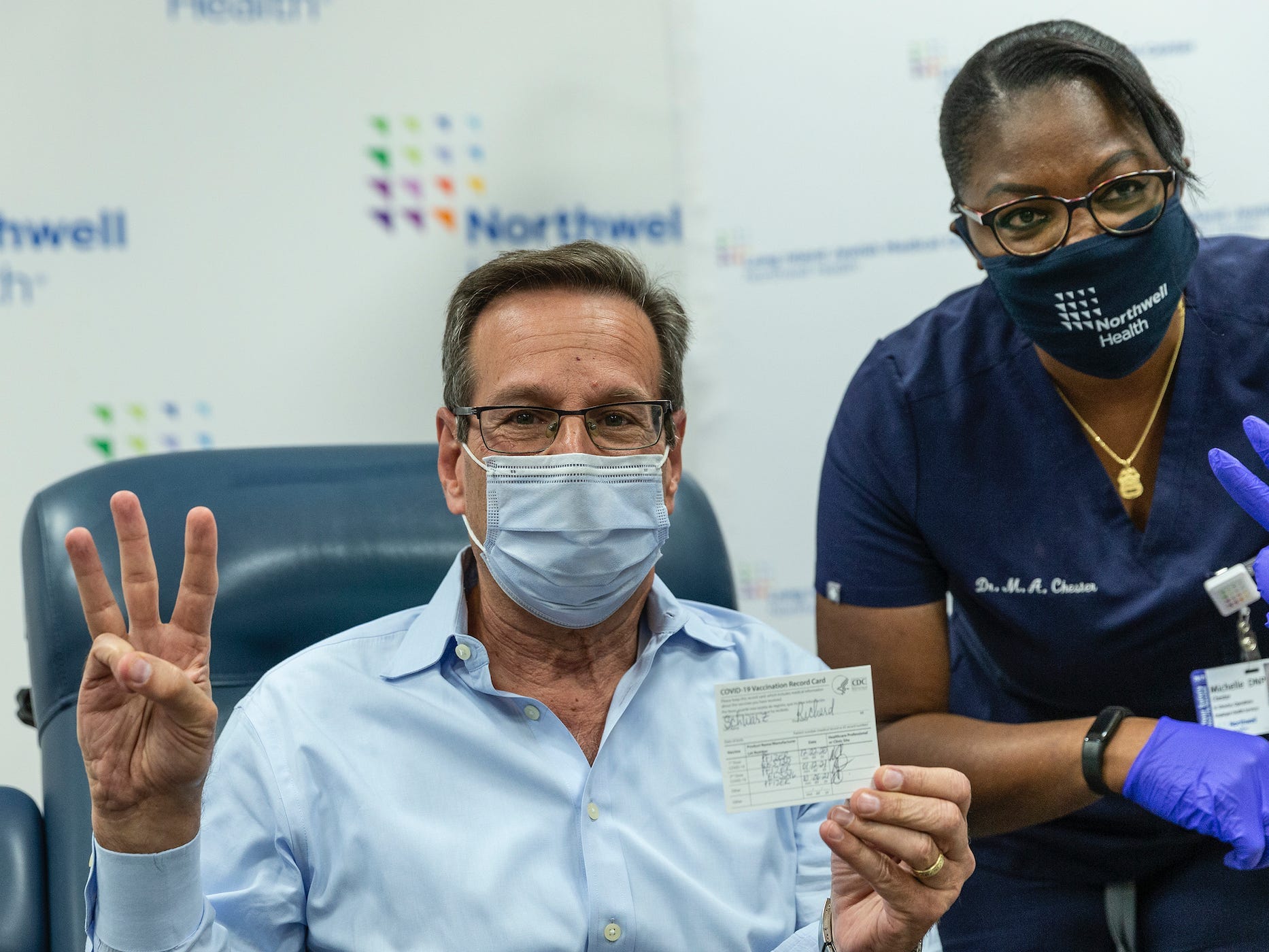 a man holds up three fingers, and his filled out CDC vaccine card, after getting a booster shot.