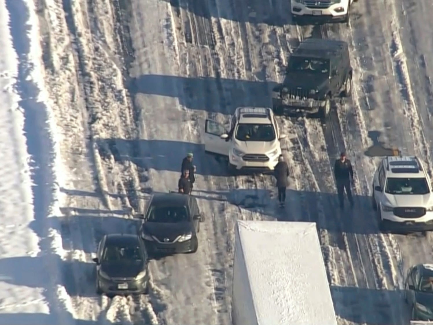 An aerial image of cars stood still on a frozen road and drivers standing beside them