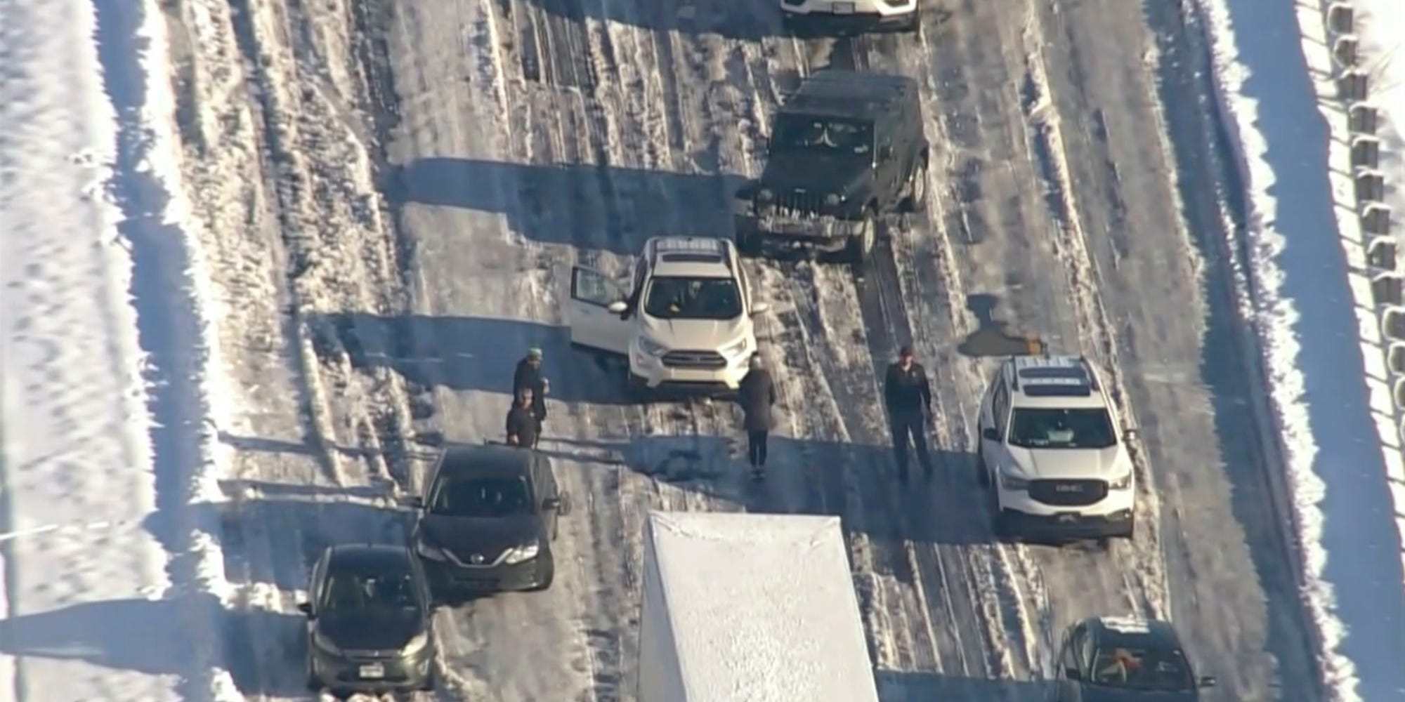 An aerial image of cars stood still on a frozen road and drivers standing beside them