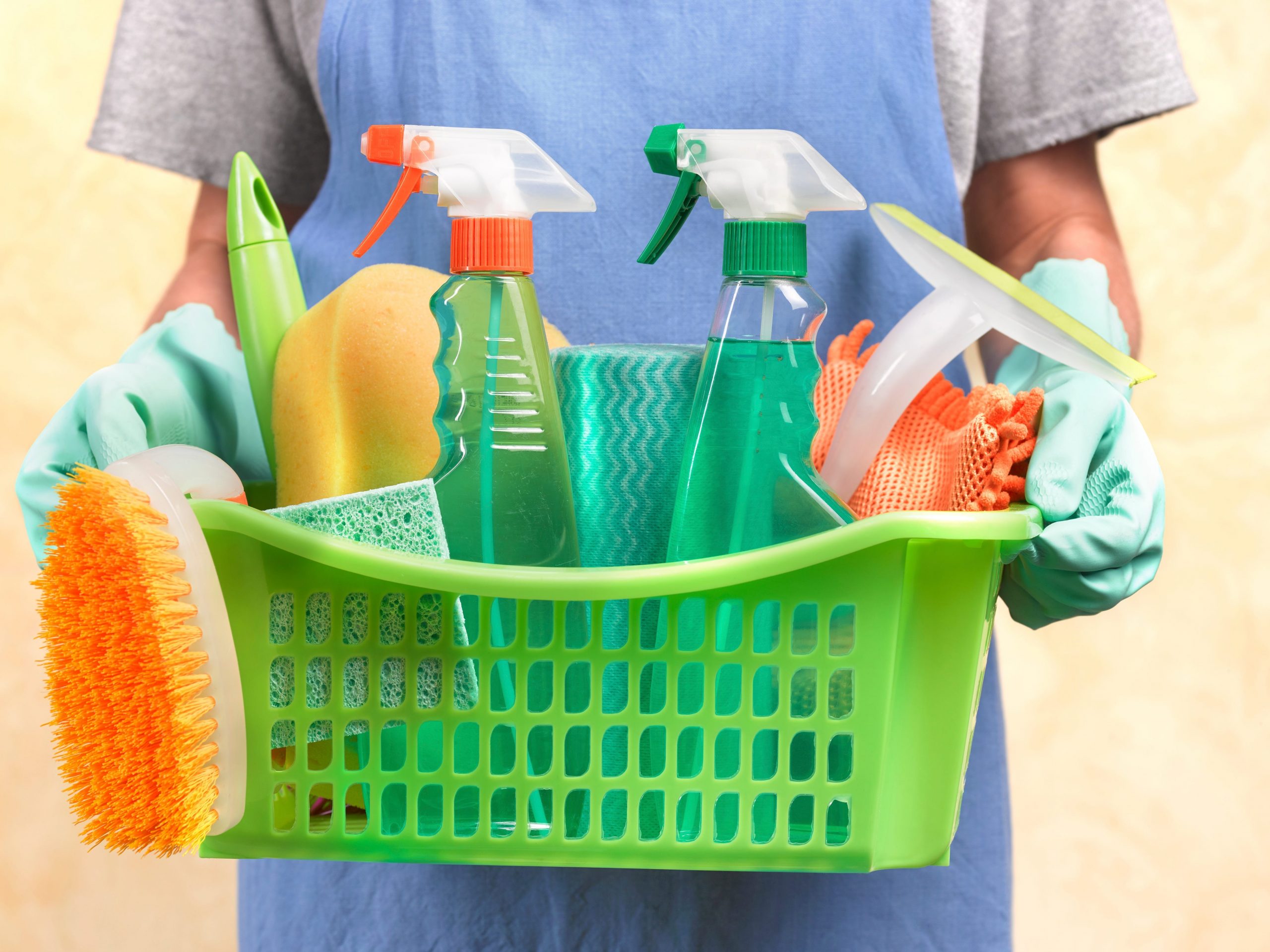 Man holding green basket with cleaning supplies.