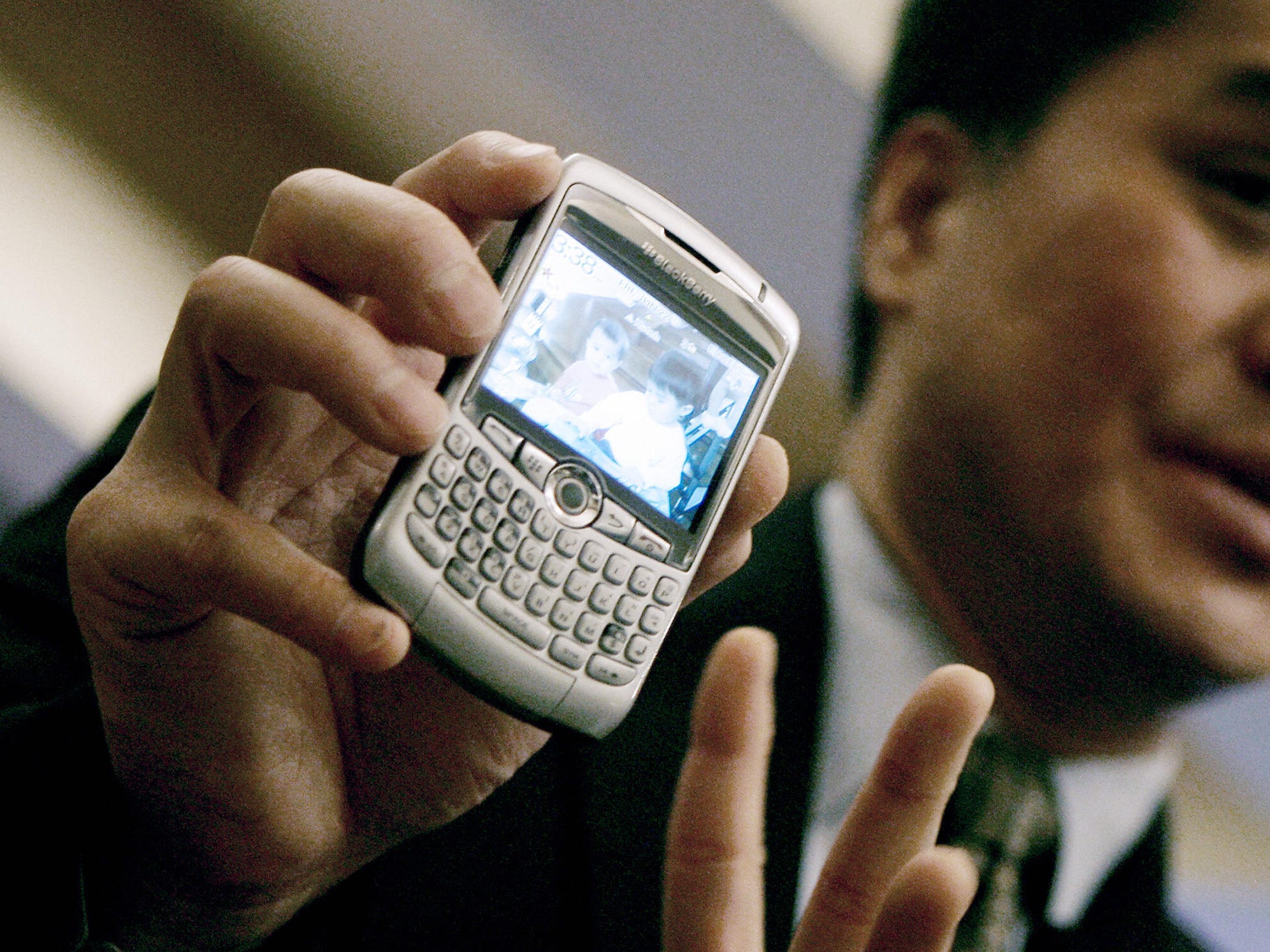 Man holds up a silver Blackberry phone