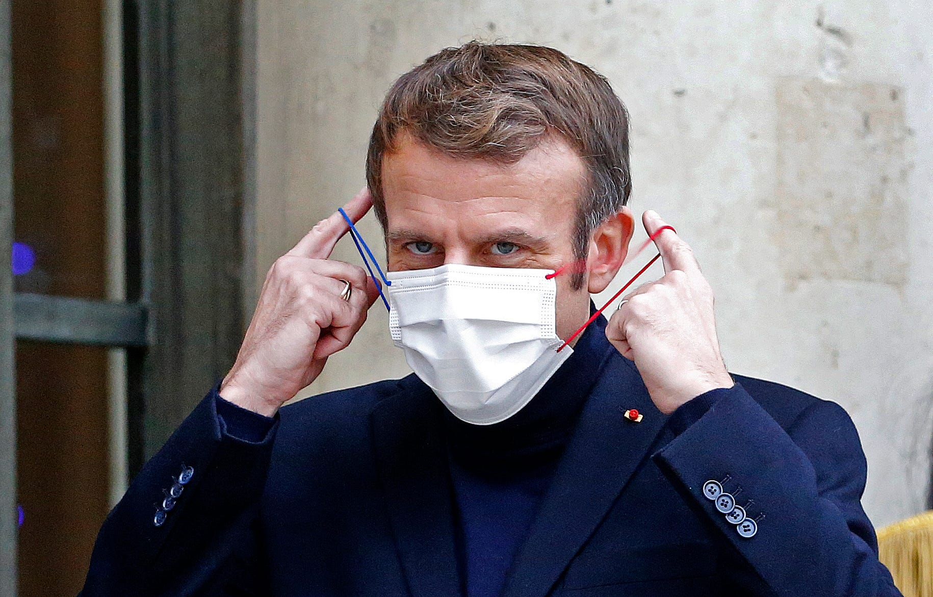 French President Emmanuel Macron takes off his protective face mask