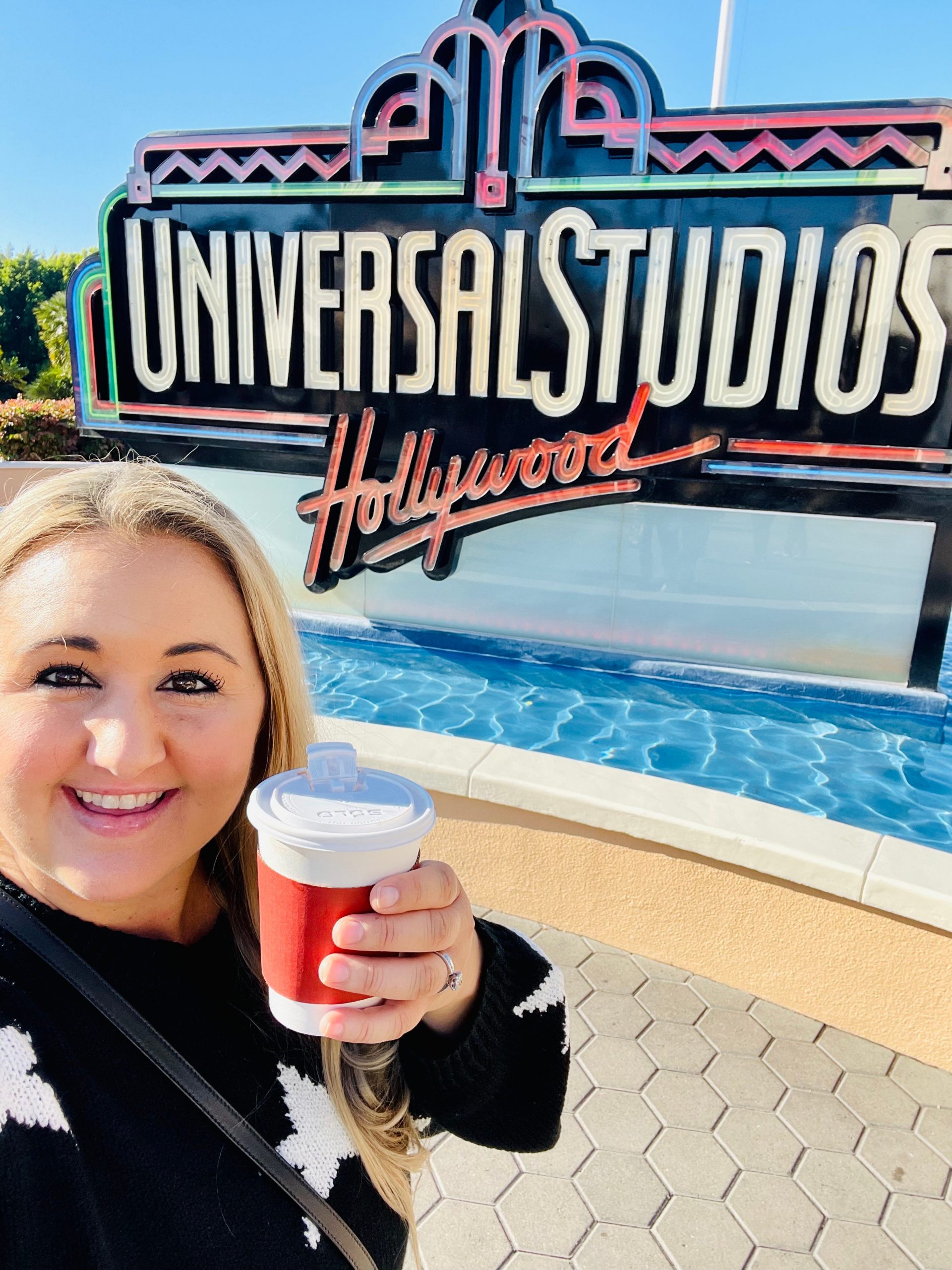 The writer posing with a cup of coffee in front of the Universal Studios sign