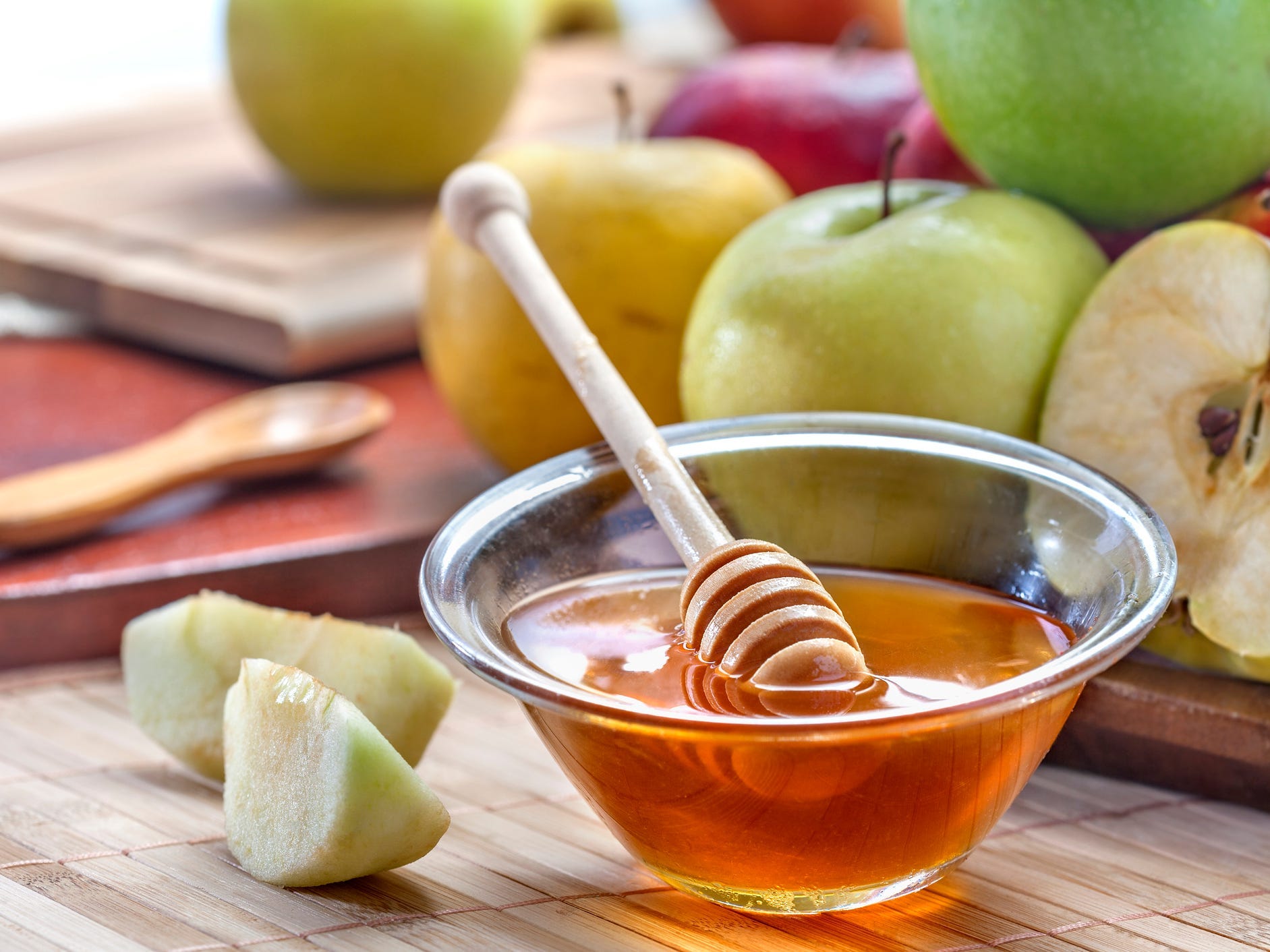 A bowl of honey with two green apple slices next to it