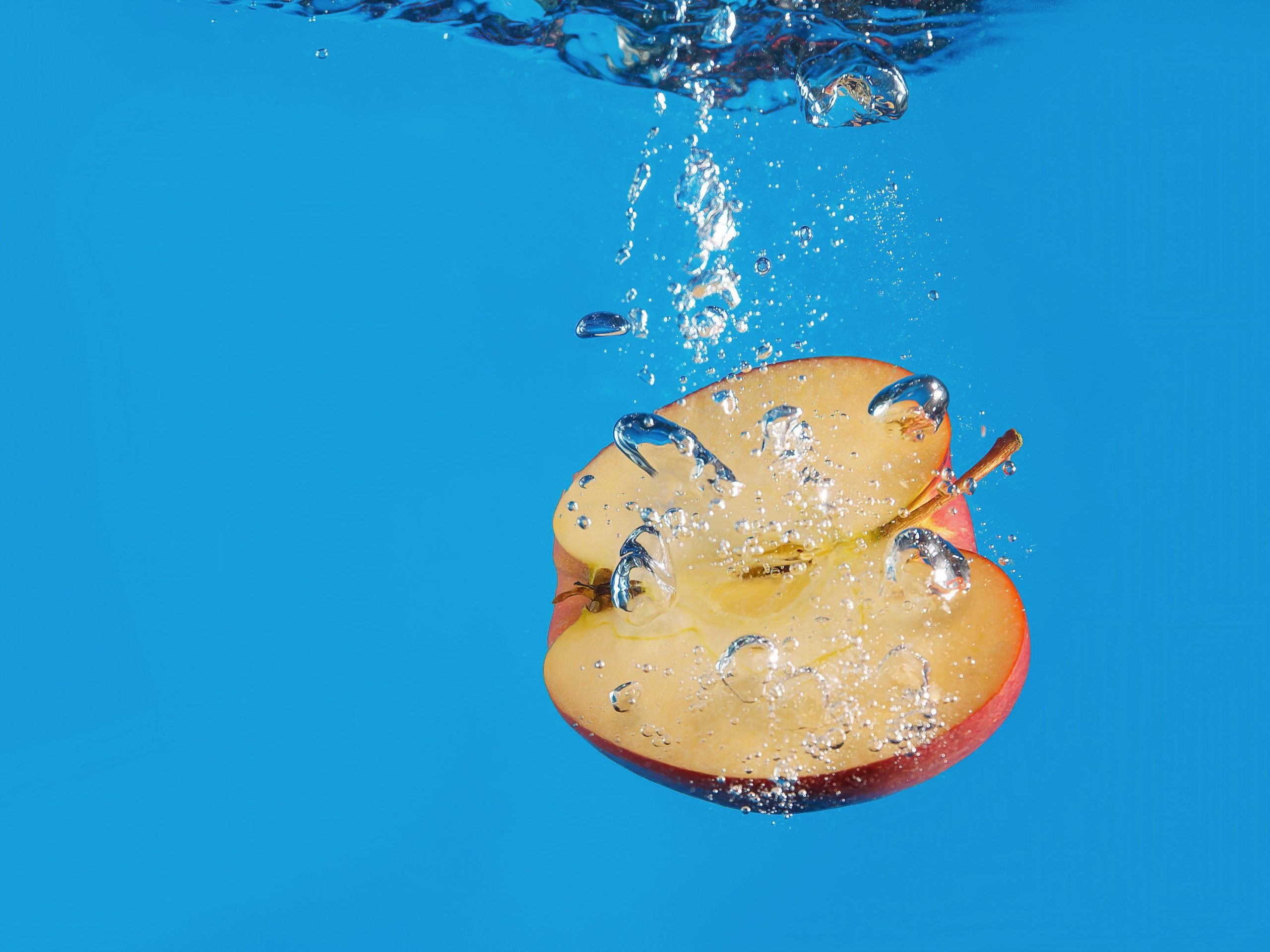 Half an apple sinking into water on a blue background