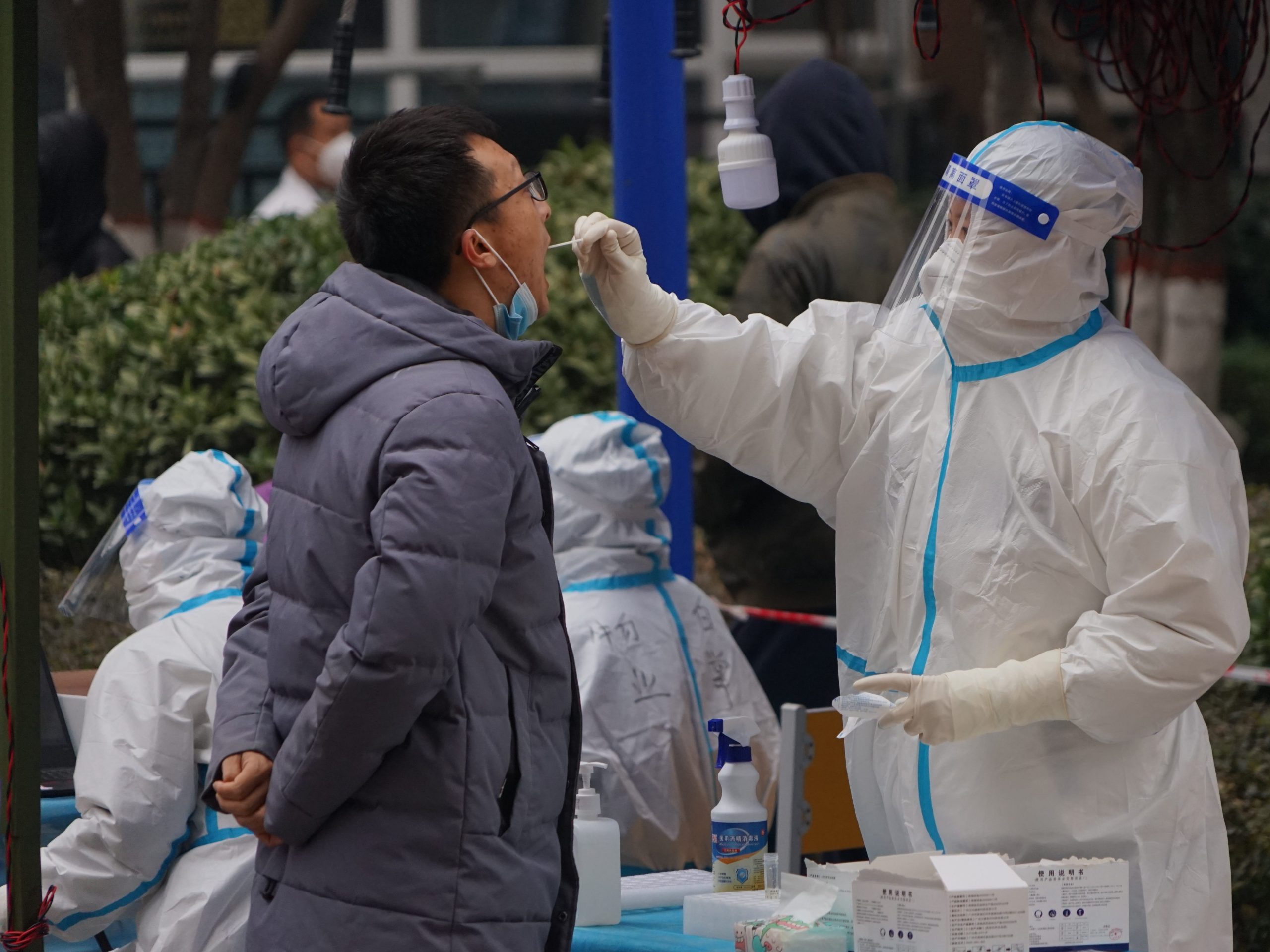 A man in full protective gear (R) administers a COVID-19 nucleic acid test to a Xi'an resident (L) dressed in a grey jacket.