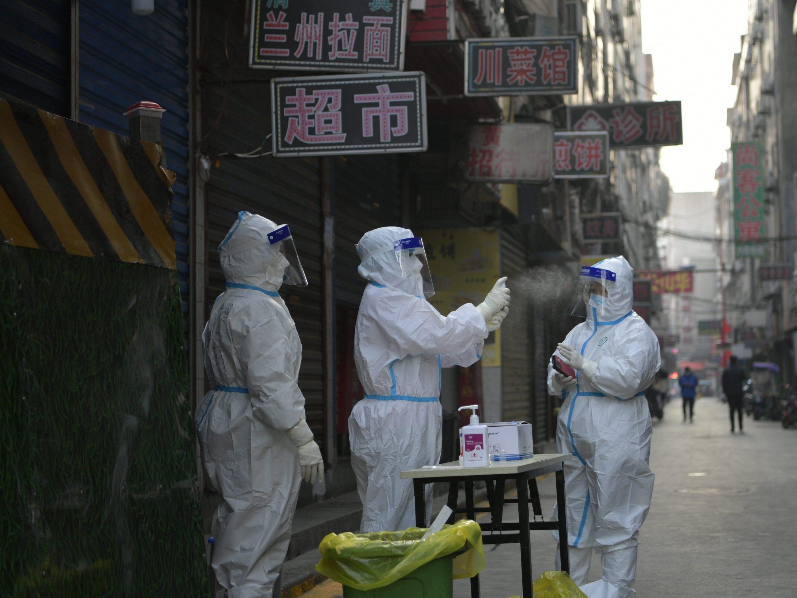 Three workers standing on a deserted street in Xi'an, China, wearing full protective gear.
