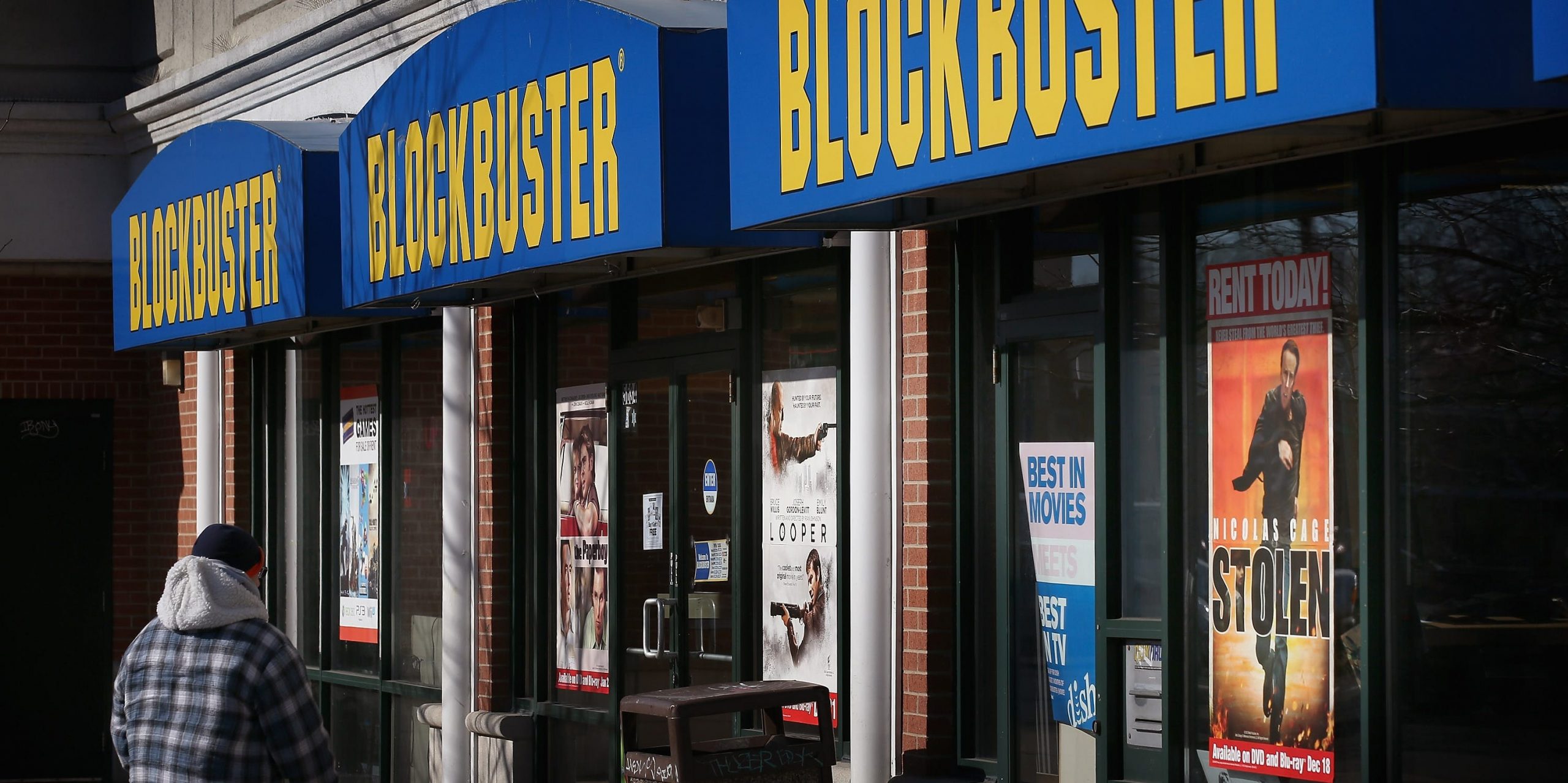 A man walks in front of a Blockbuster video store.