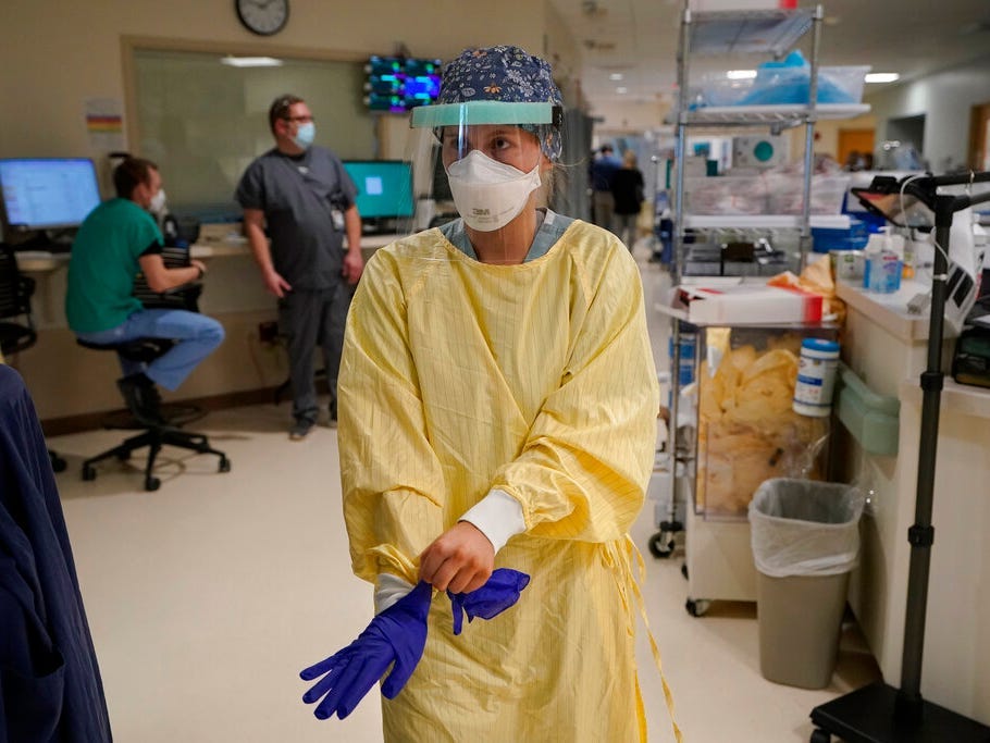Registered Nurse Morgan Flynn puts on gloves while wearing PPE before entering a patient's room in the ICU.