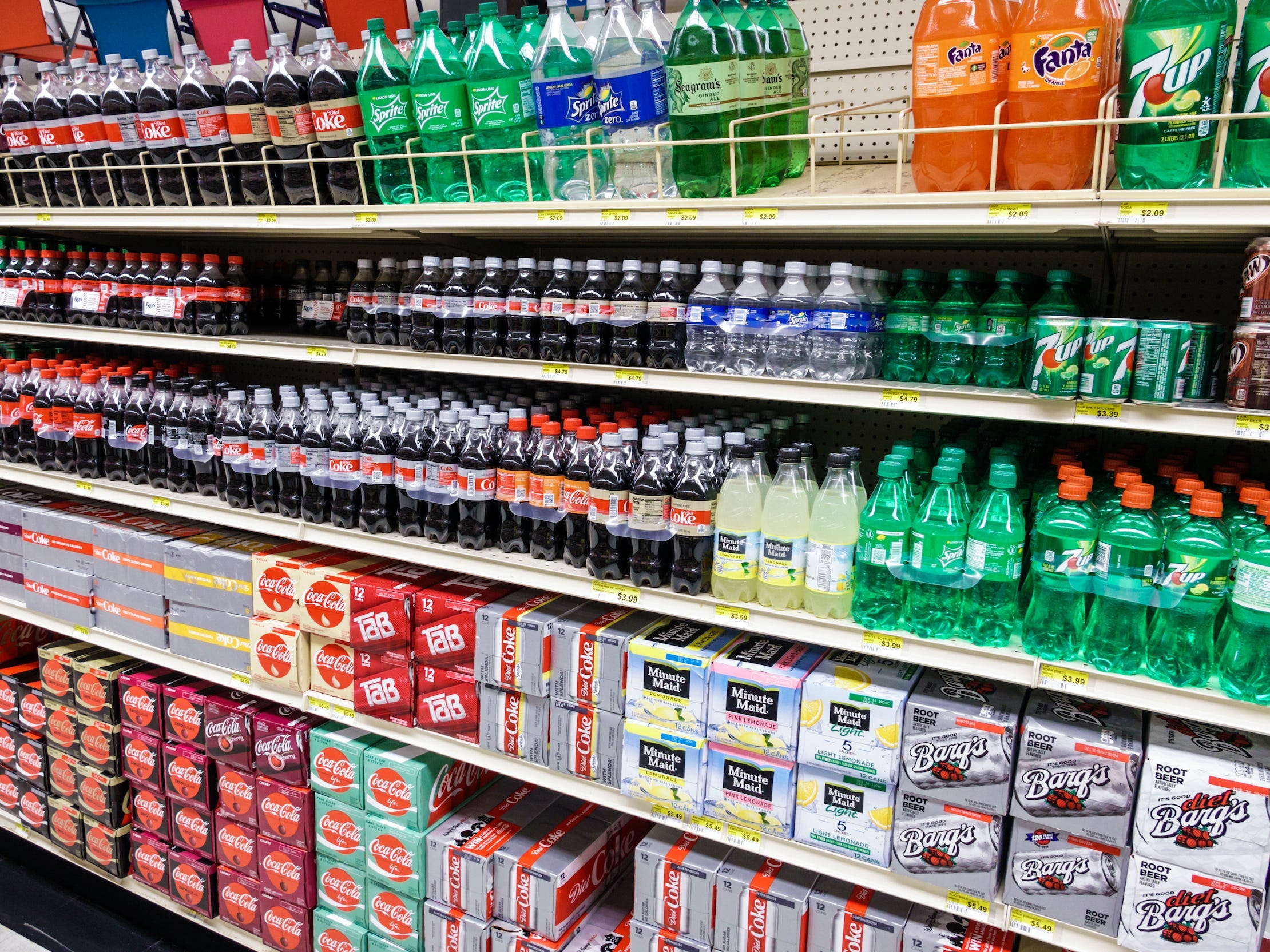 A grocery store aisle with soda brands including Coca-Cola, Sprite, 7 Up, and more