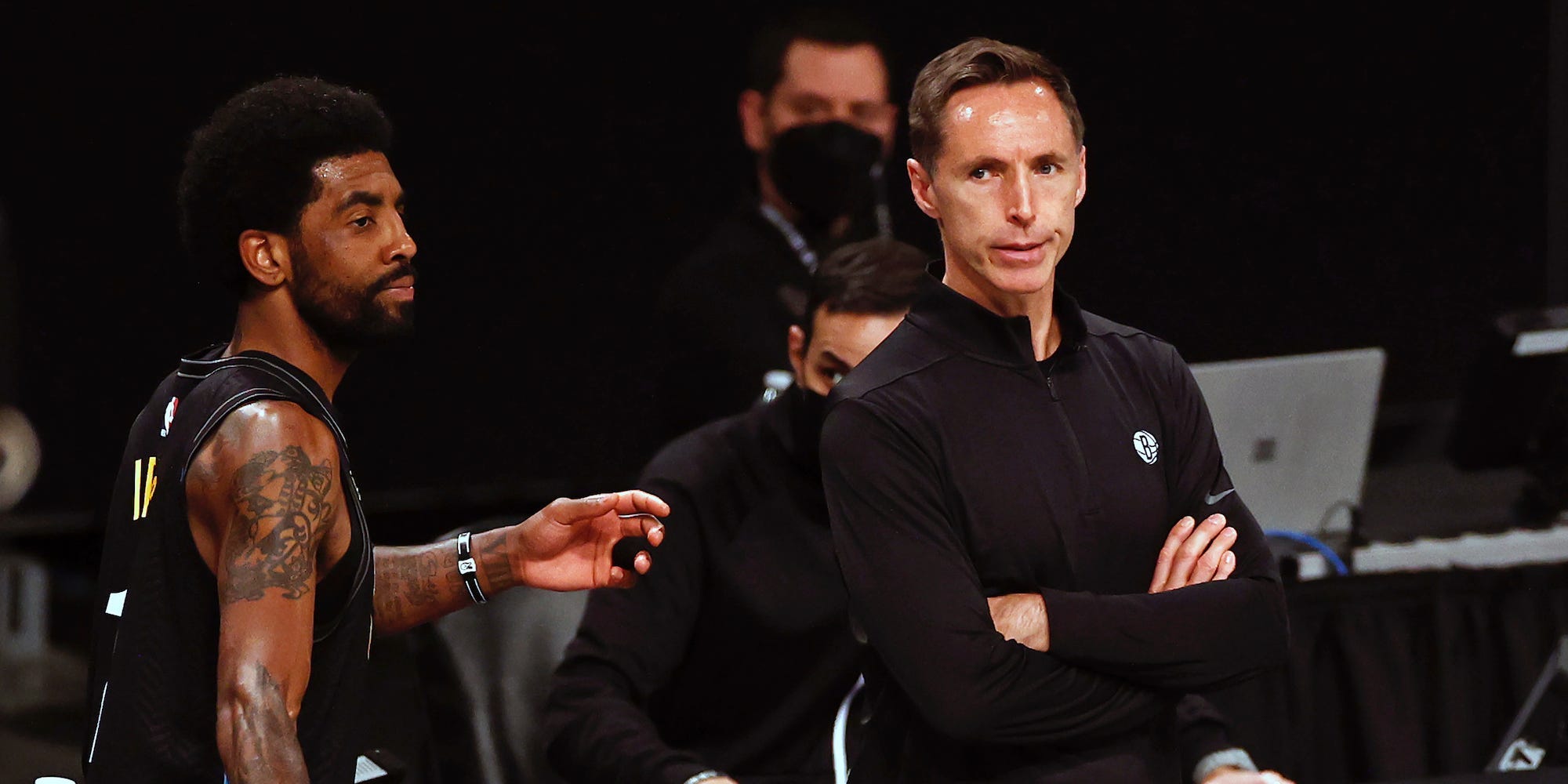 Kyrie Irving walks by Steve Nash as Nash stands with his arms crossed.