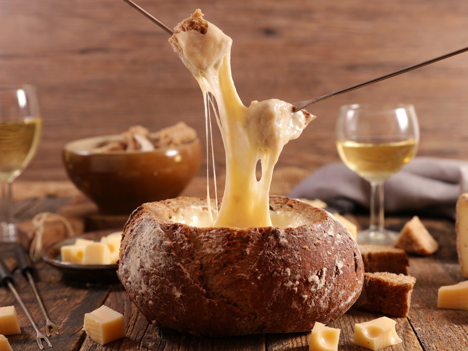 A bread bowl filled with cheese fondue with two pieces of bread being dipped into the cheese