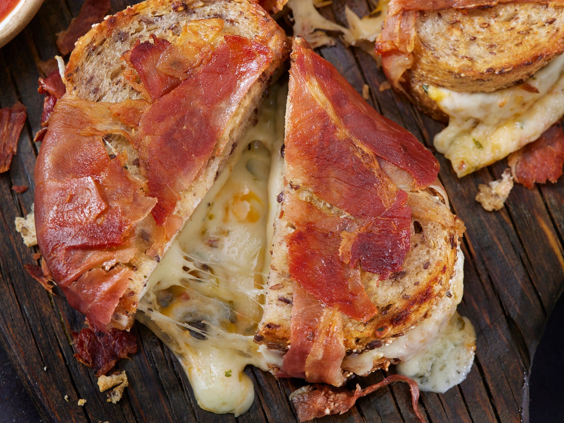 A prosciutto-wrapped grilled cheese cut in half with mozzarella oozing out