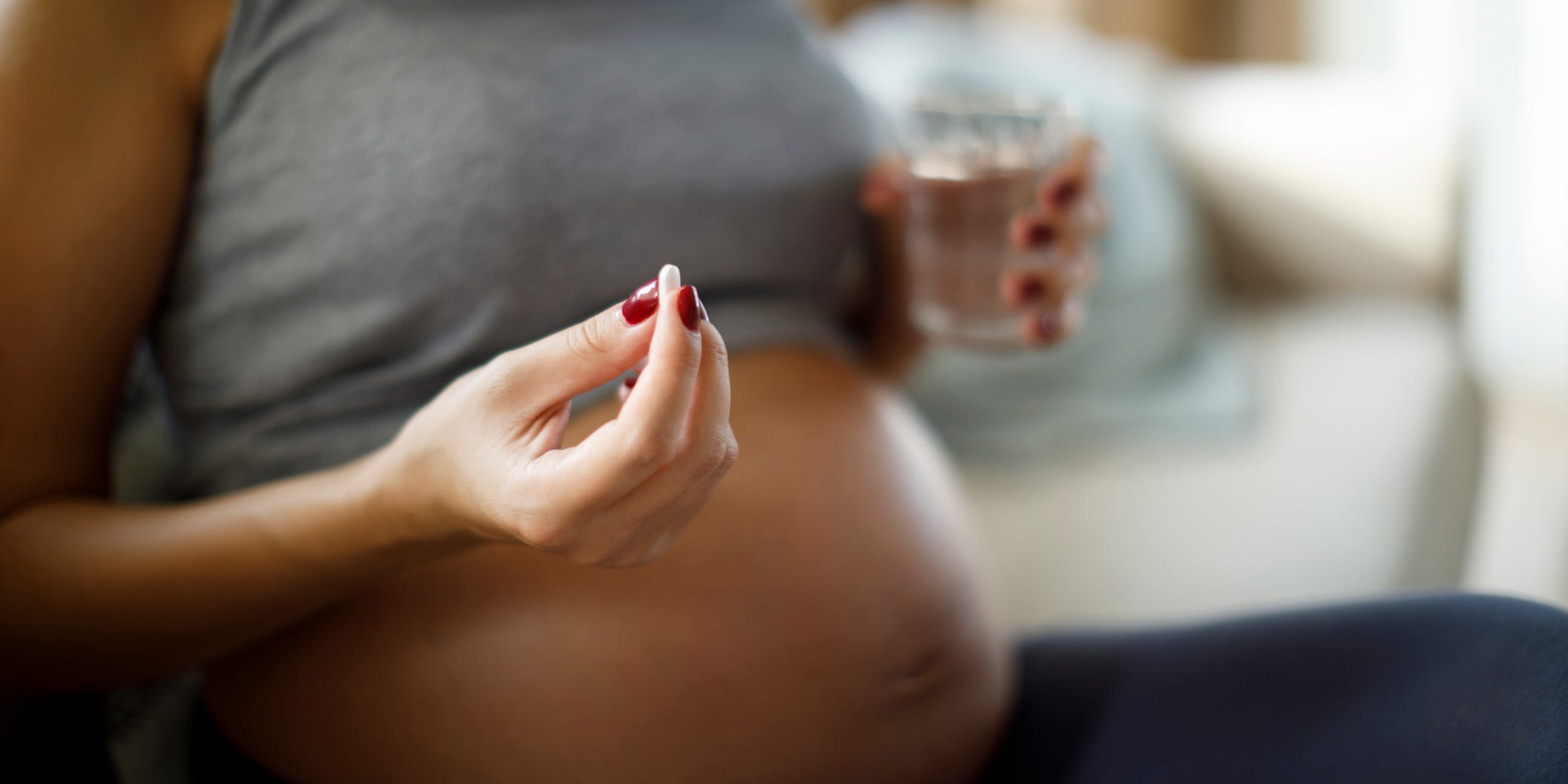 A pregnant woman holds a pill in her hand with a glass of water.