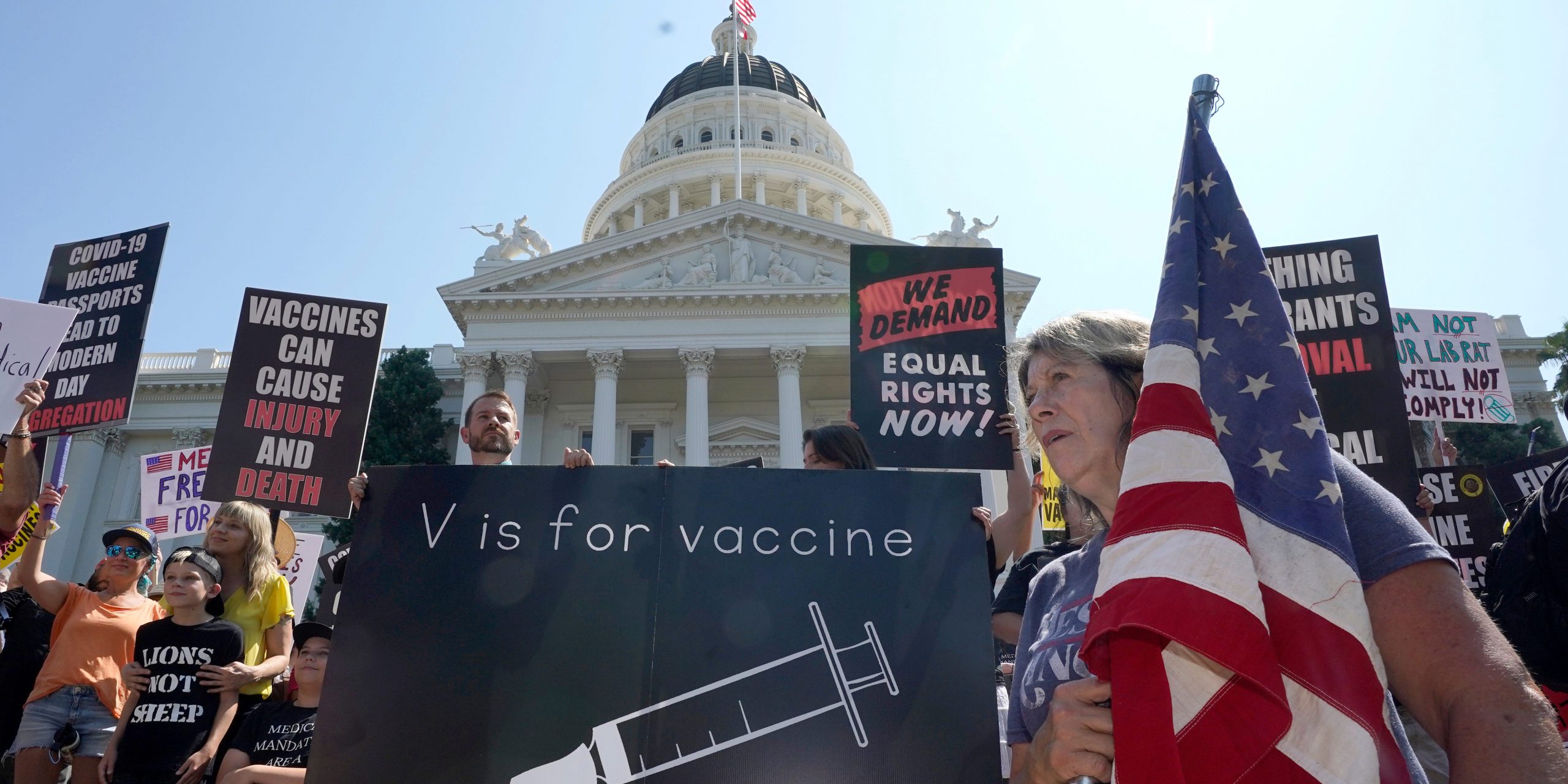 Protesters opposing vaccine mandates gather with signs and flags in front of the Capitol.