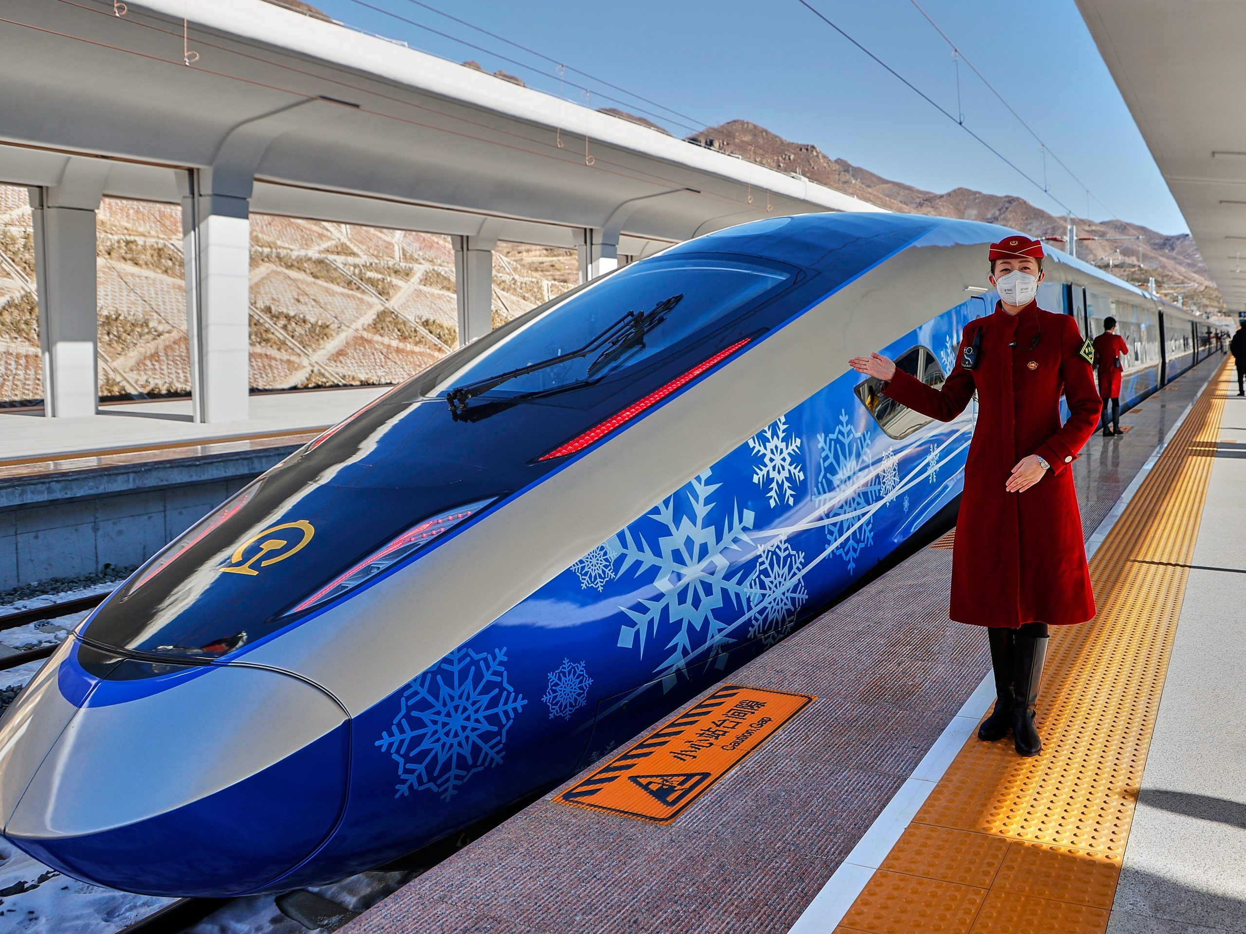 A train attendant poses beside an intelligent Fuxing bullet train decorated with a Winter Olympics-themed coating at Chongli Railway Station on January 6, 2022 in Zhangjiakou, Hebei Province of China.