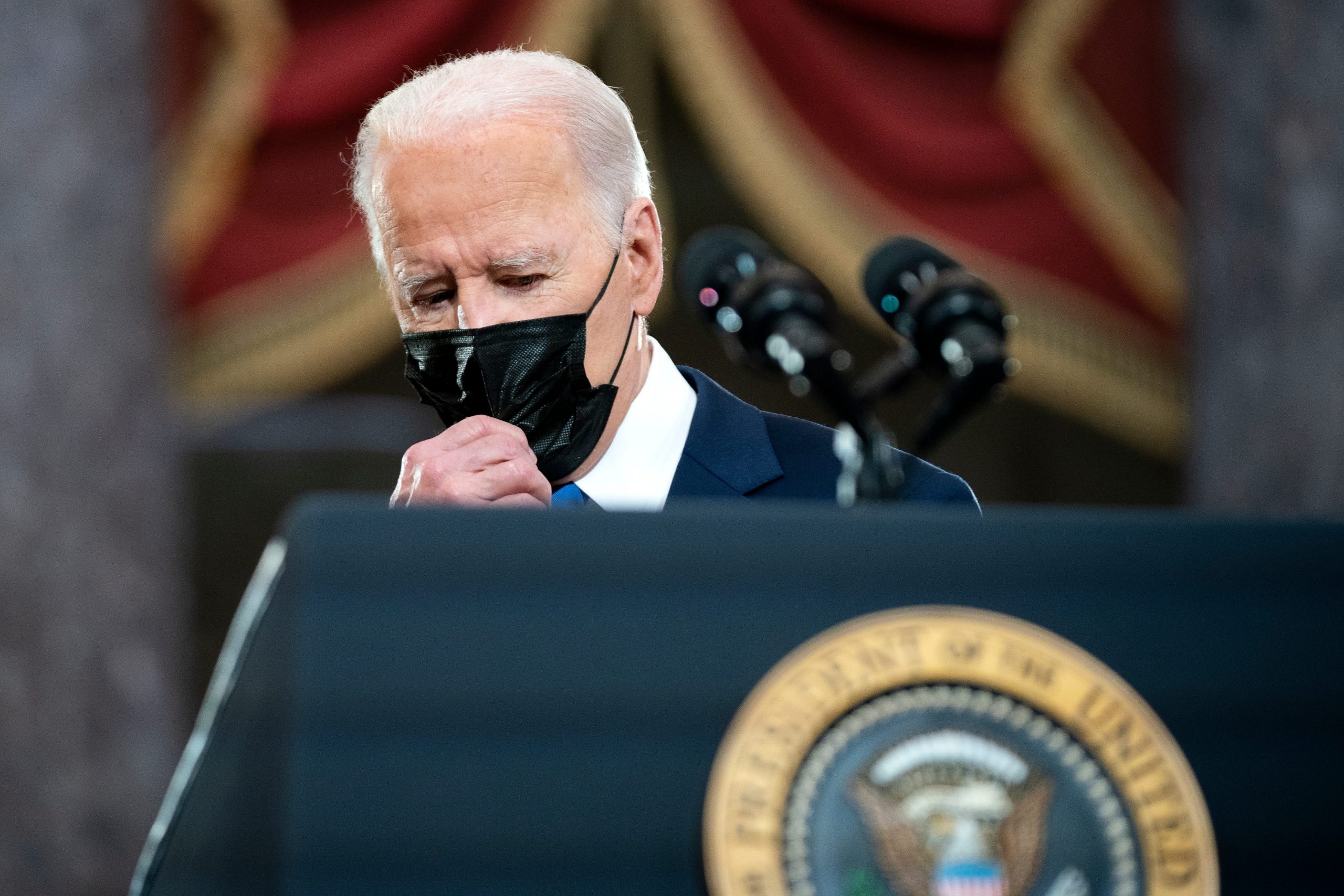 US President Joe Biden adjusts his mask as he stands on a podium