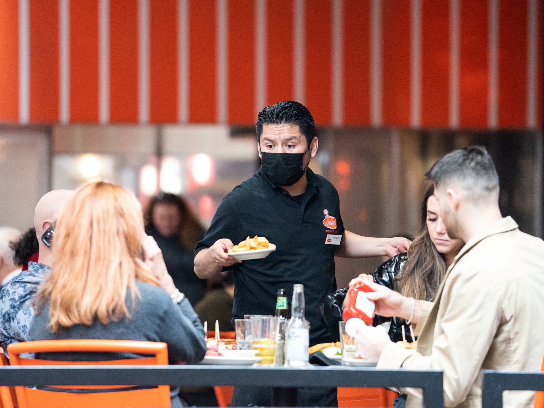 A waiter wearing a mask serves food to a table of people in New York City.