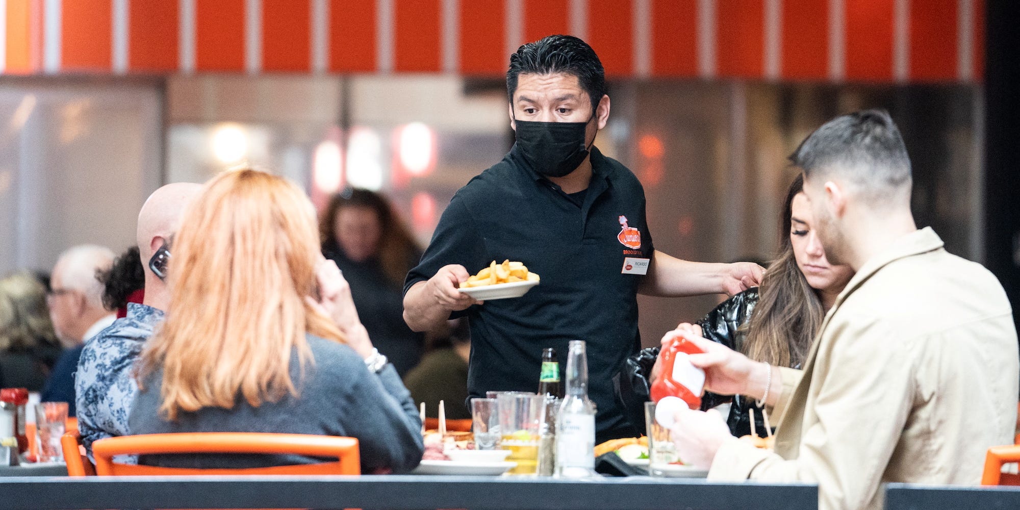 A waiter wearing a mask serves food to a table of people in New York City.