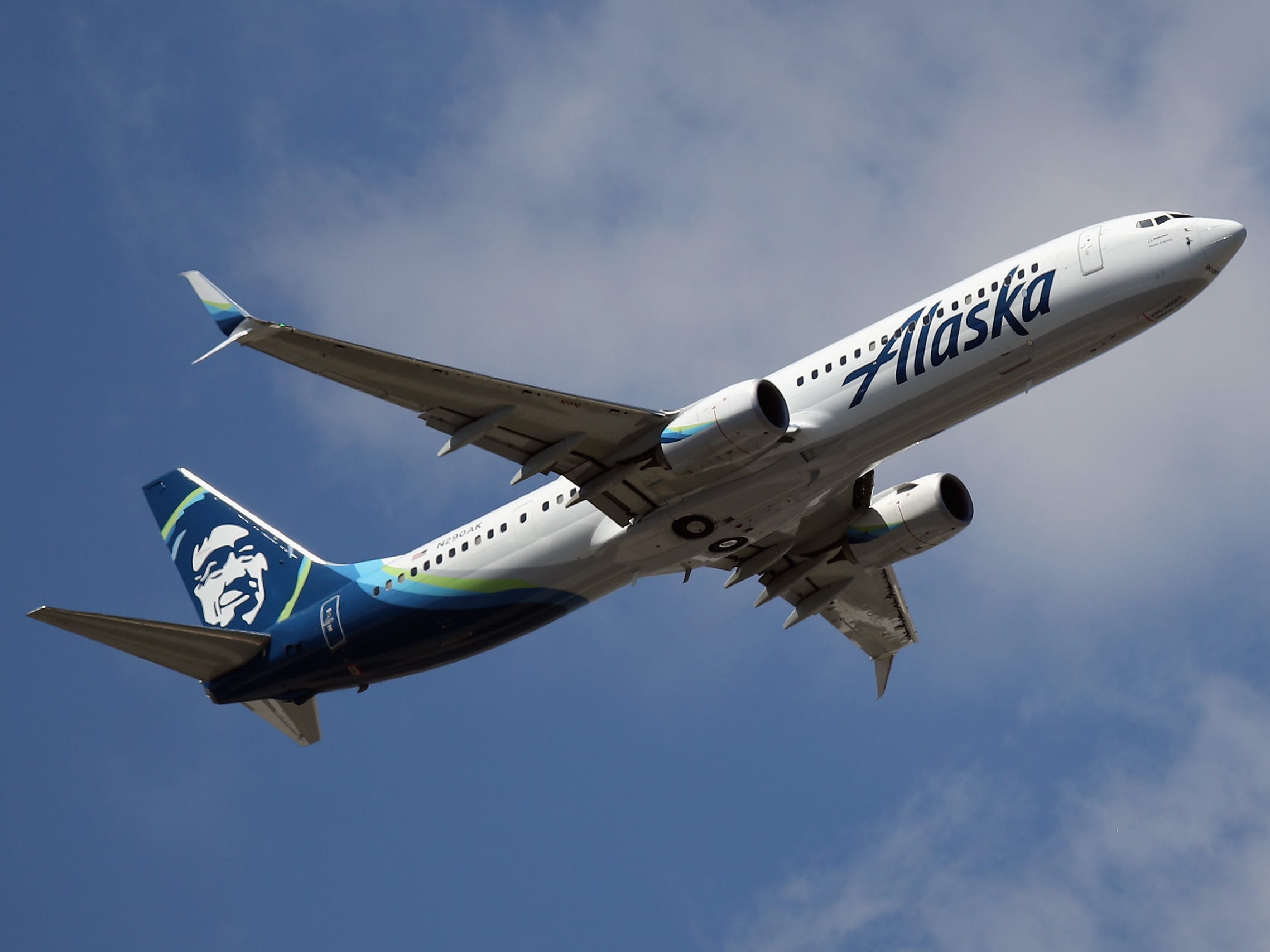 An Alaska Airlines airplane taking off against a blue sky with white clouds.