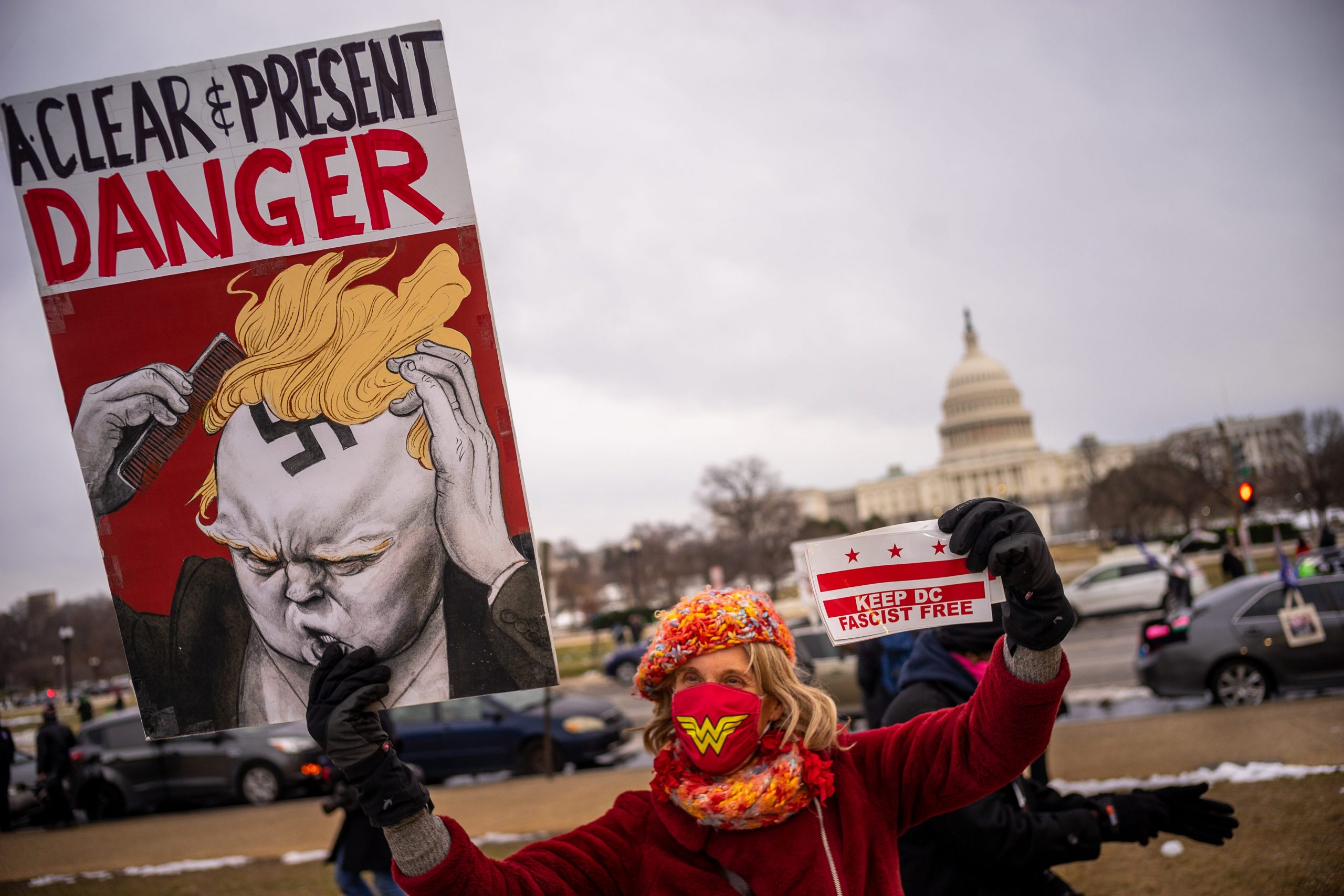 A woman holds a sign with the words "A Clear and Present Danger" and an image that appears to combine Donald Trump and Hitler.