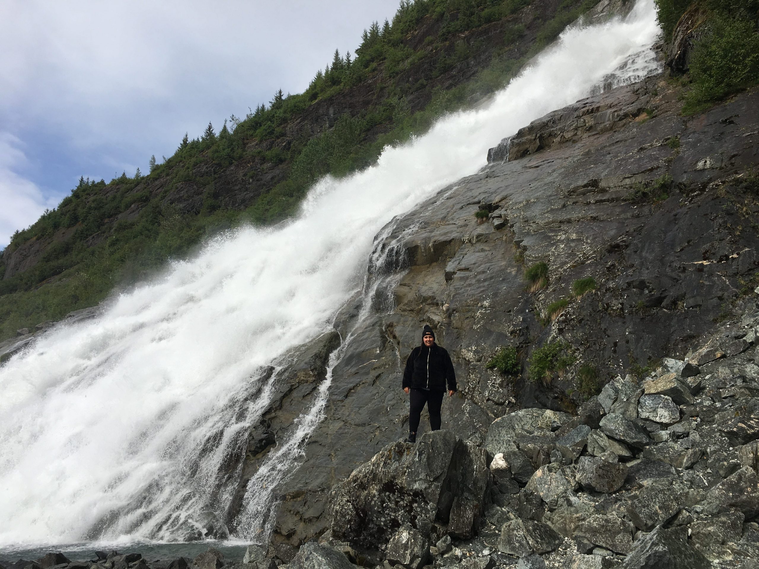 The writer standing on a rock formation with a waterfall in the background
