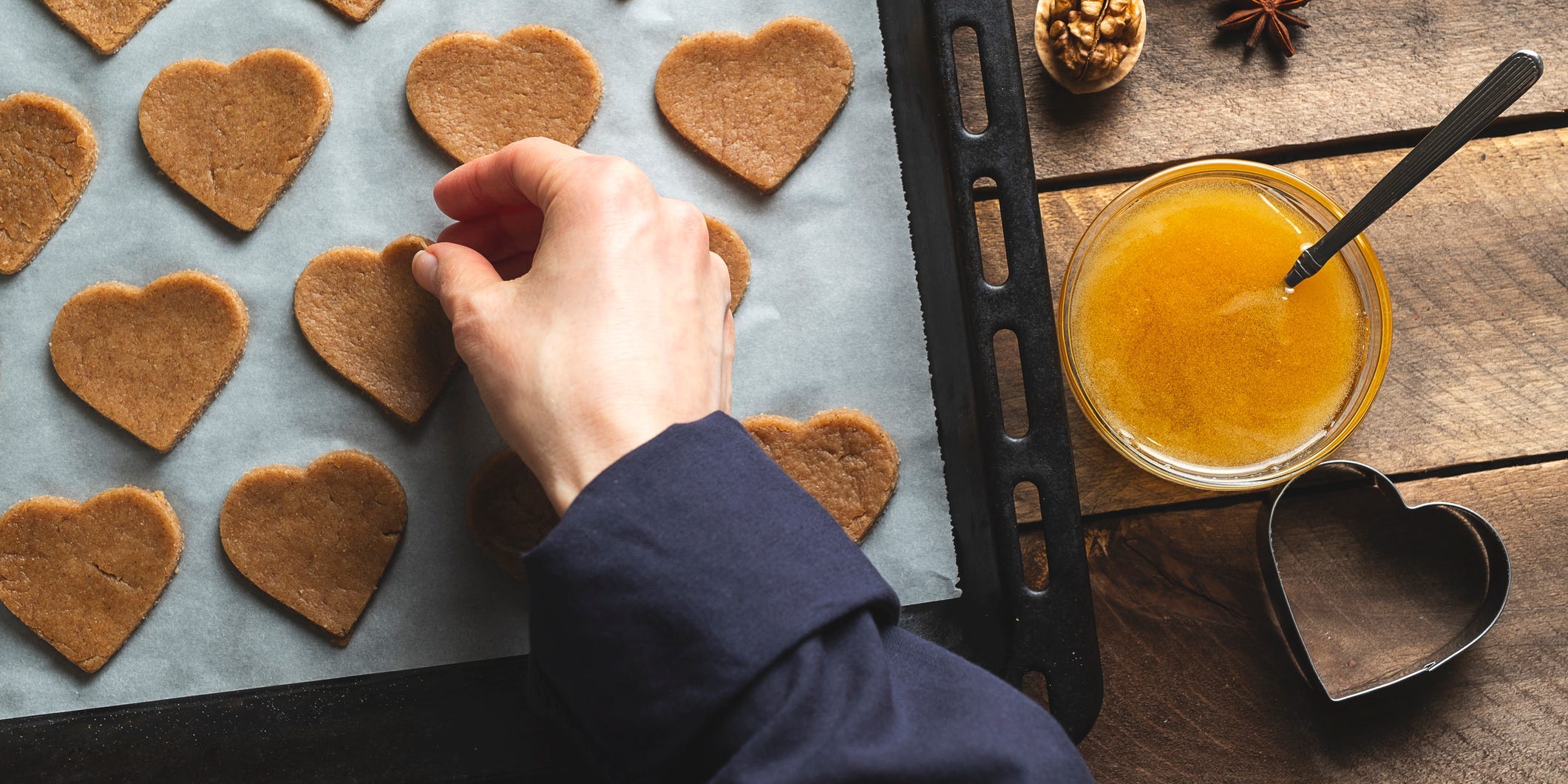 A hand placing heart-shaped cookie dough onto a parchment-lined baking sheet