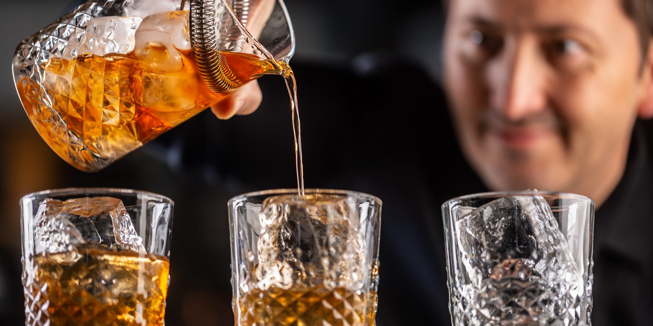 A bartender pouring bourbon into ornamental glasses.