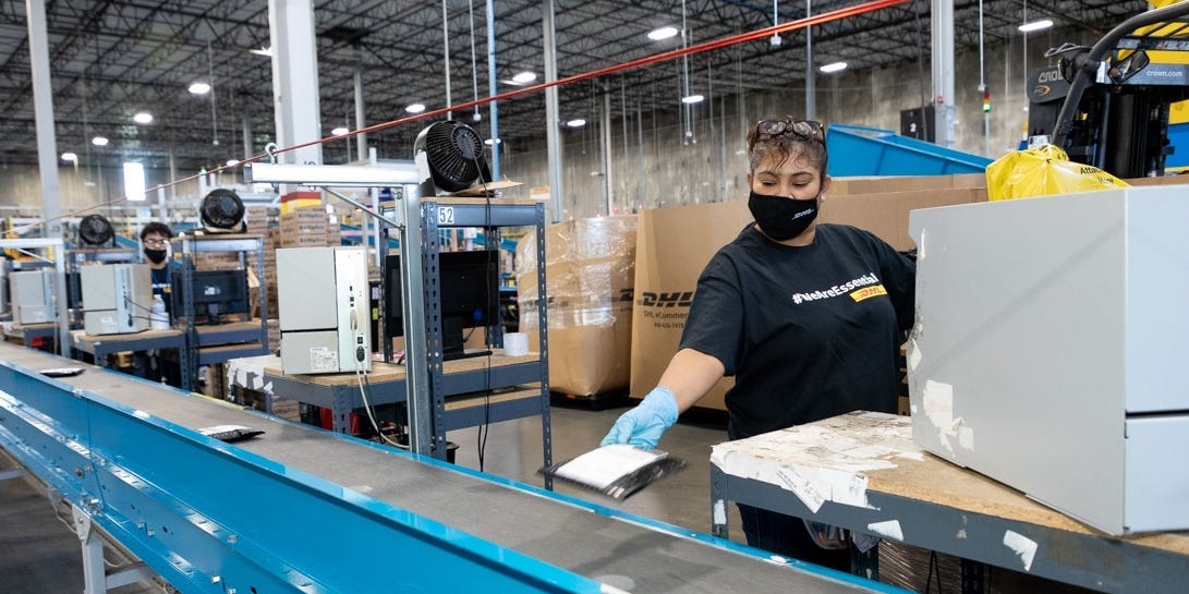 DHL workers place packages on a conveyor belt.