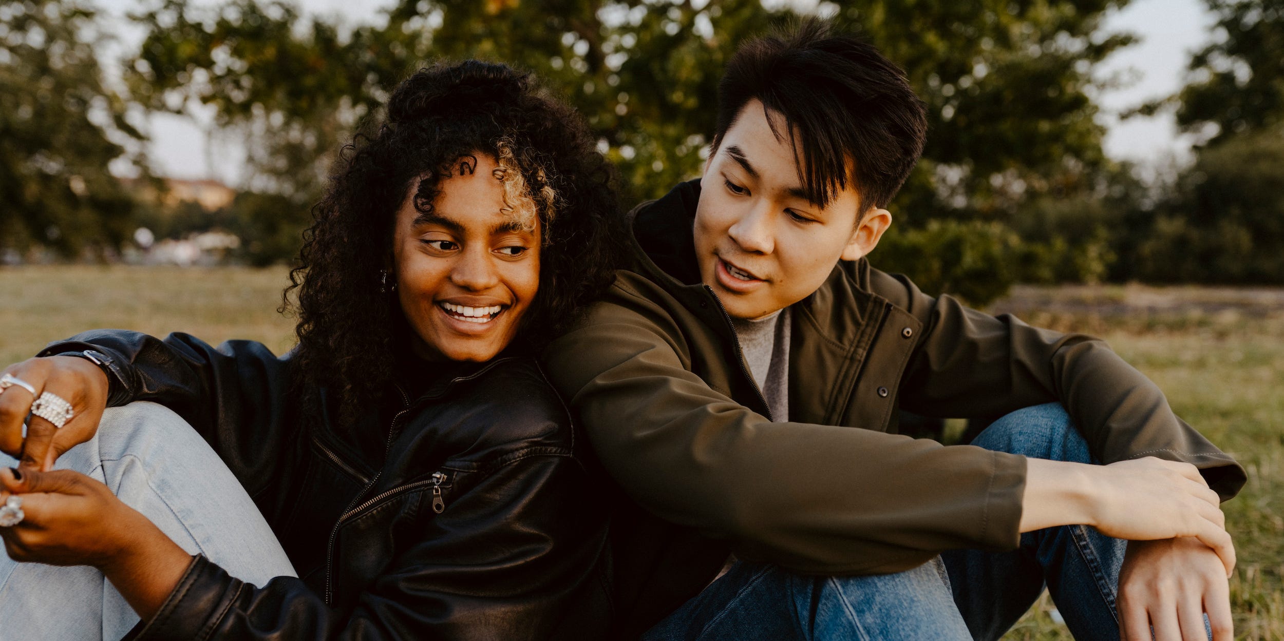 Two friends chat while sitting back to back in a park.