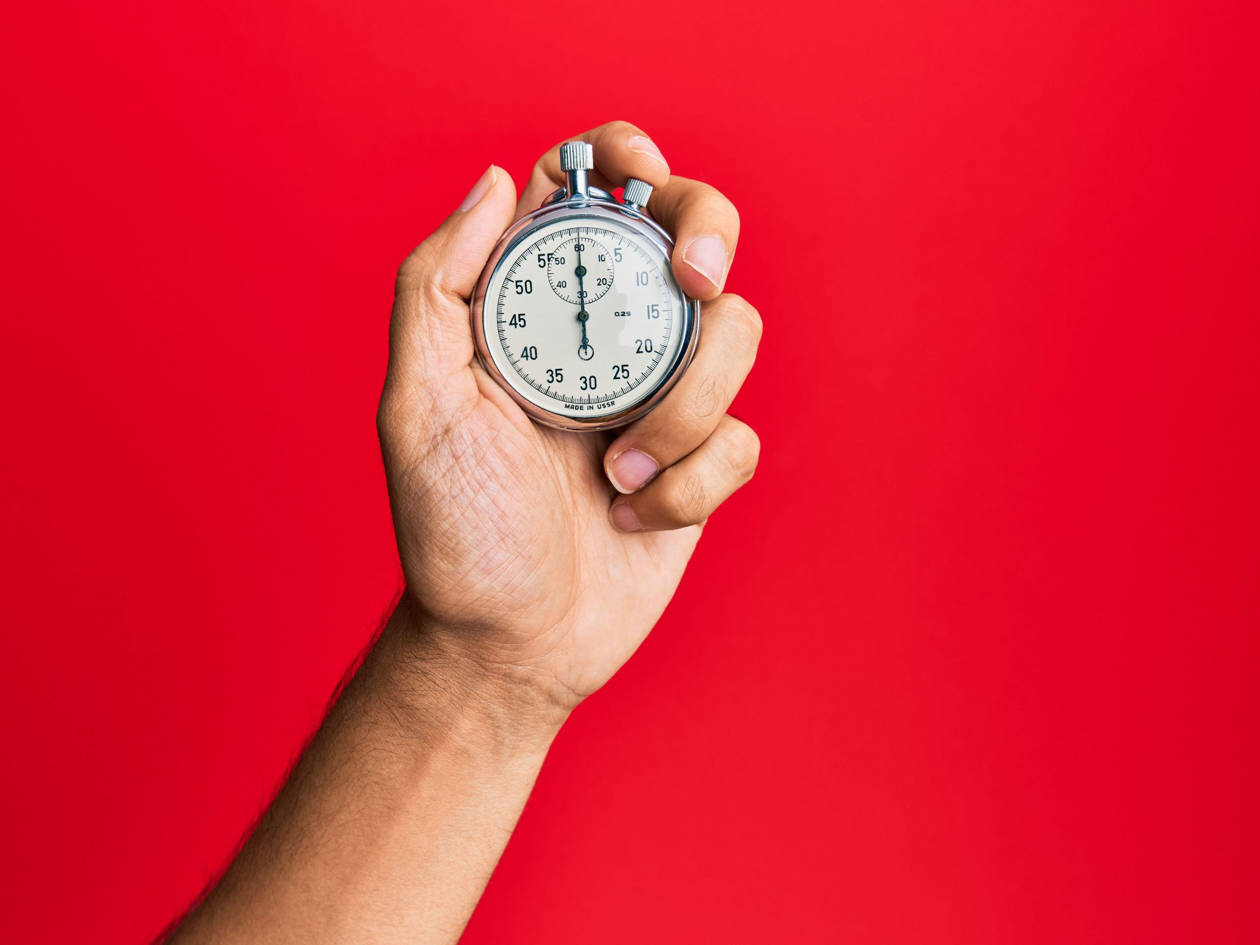 a hand holds a stopwatch against a red background
