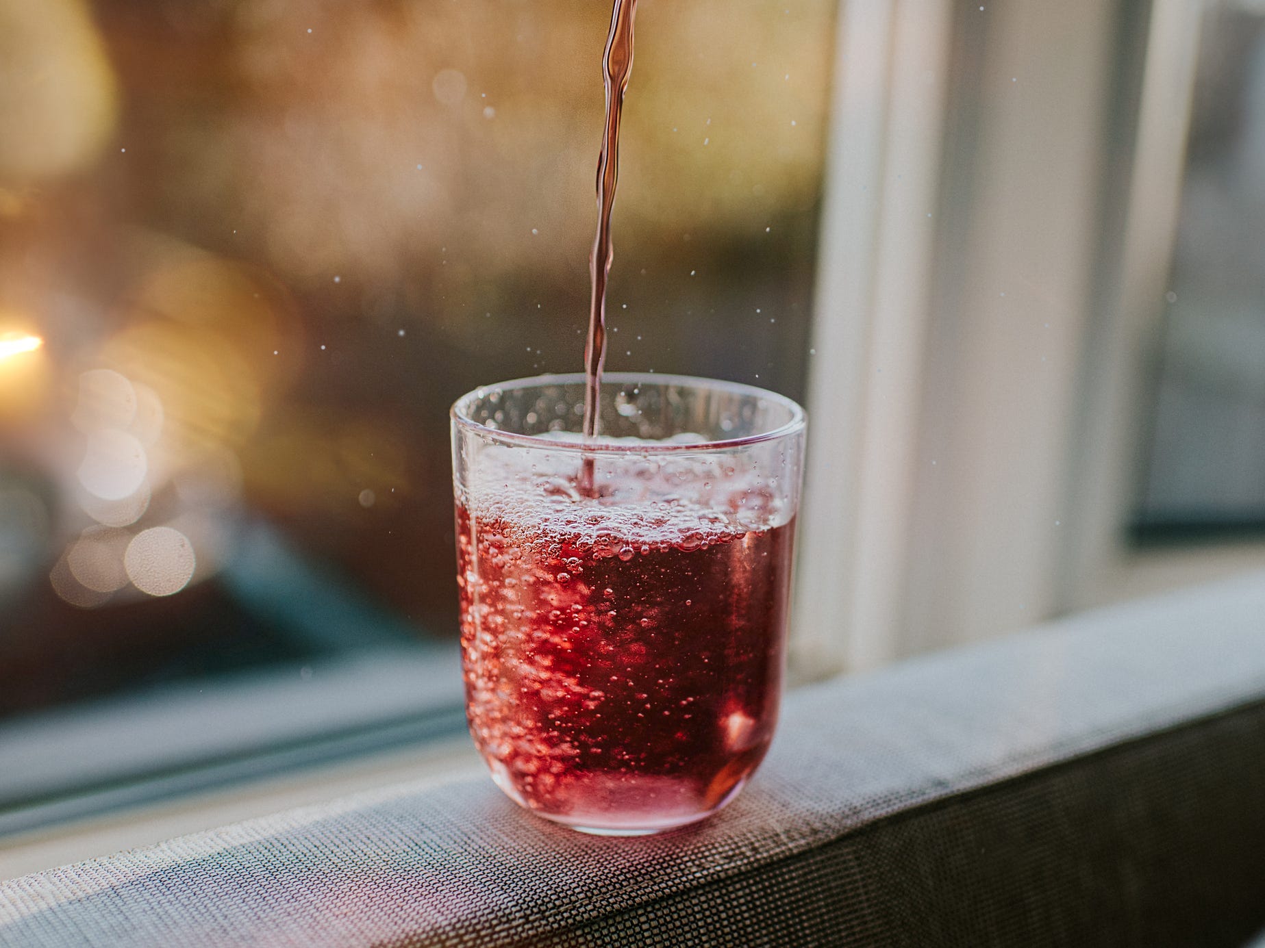 A small sized glass with a red carbonated beverage being poured into it