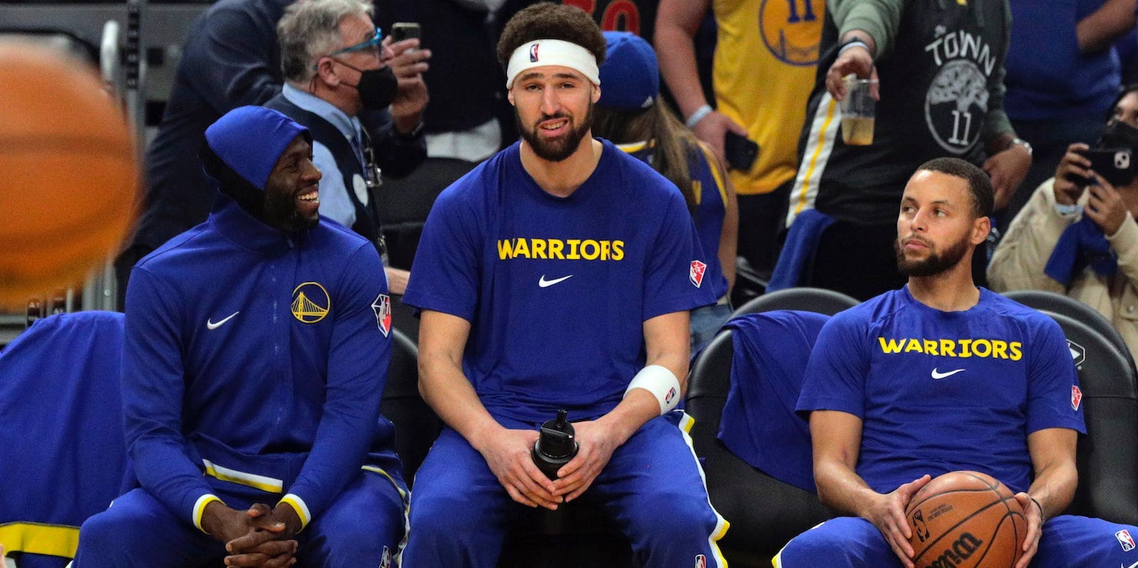Draymond Green, Klay Thompson, and Stephen Curry sit next to each other on the bench, talking, before a game in 2022.