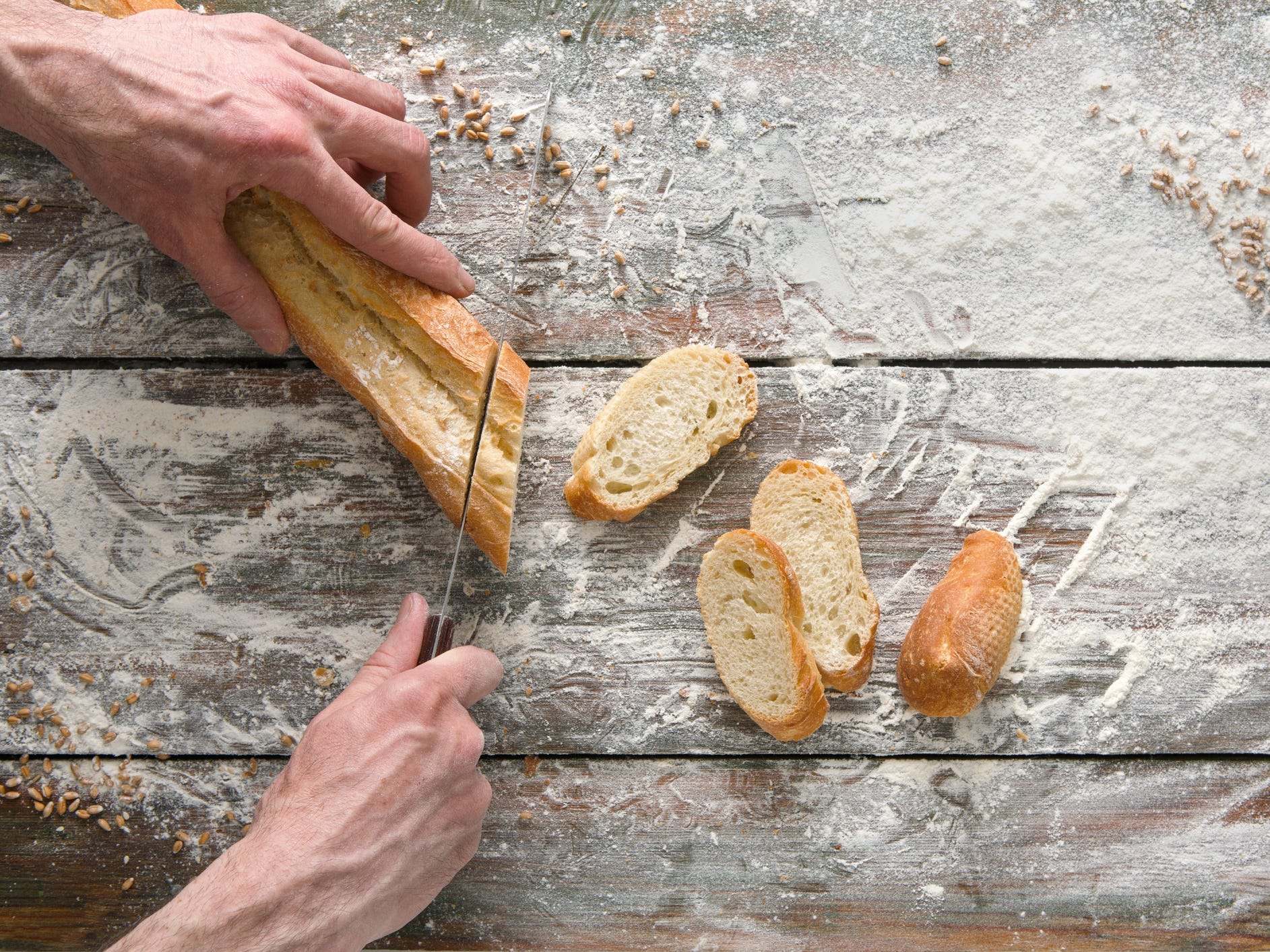 Baguette being sliced on a floured surface.