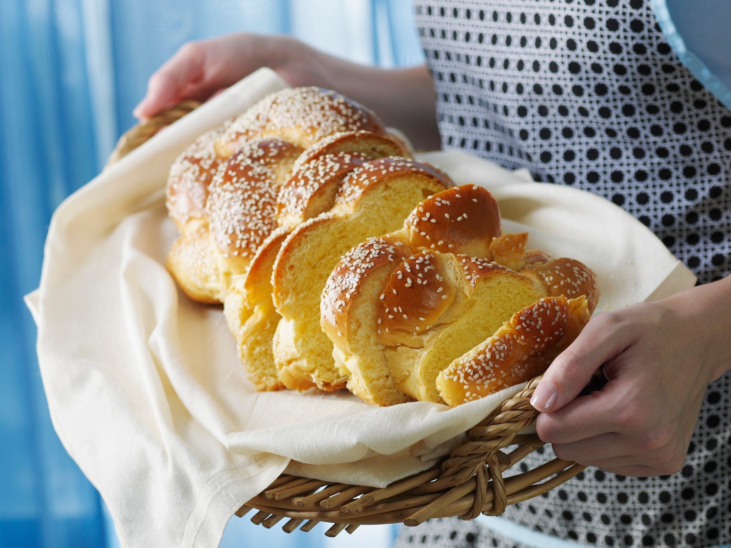 Person holding a sliced loaf of challah in a basket.